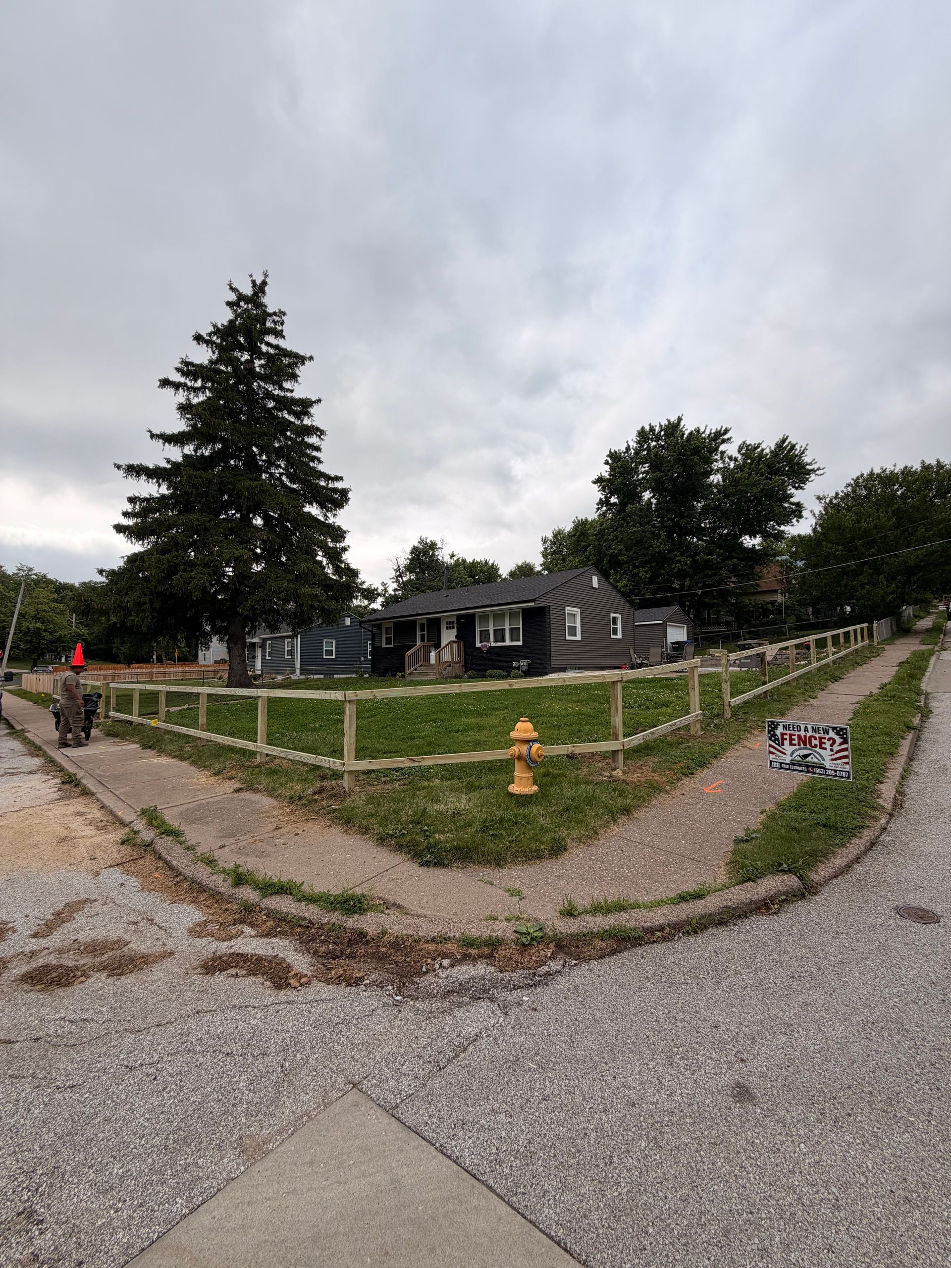 Gravel path leading to a small house and trees under a cloudy sky, with a person walking left.