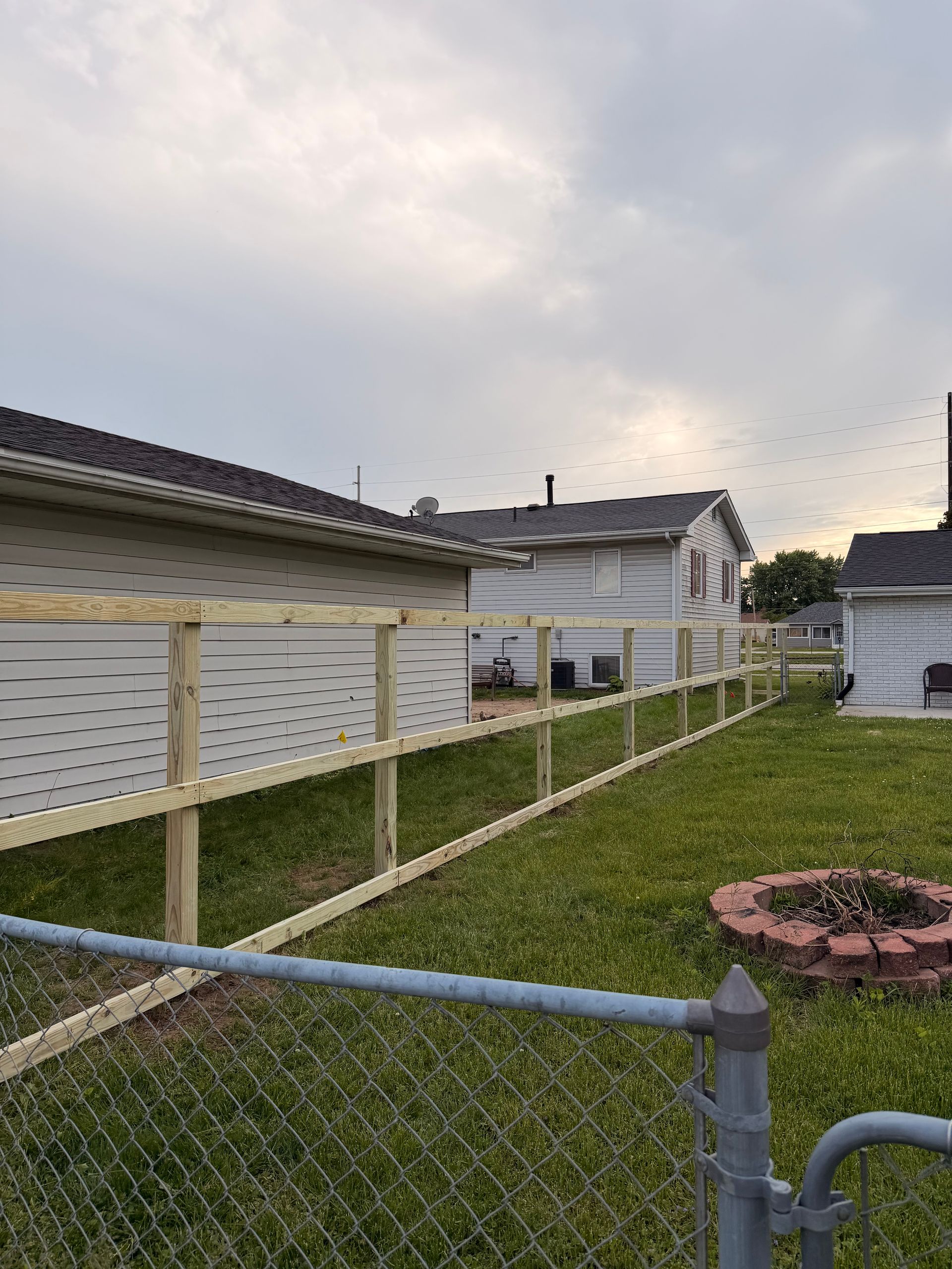 Backyard with white siding, chain-link fence, and cloudy sky at dusk
