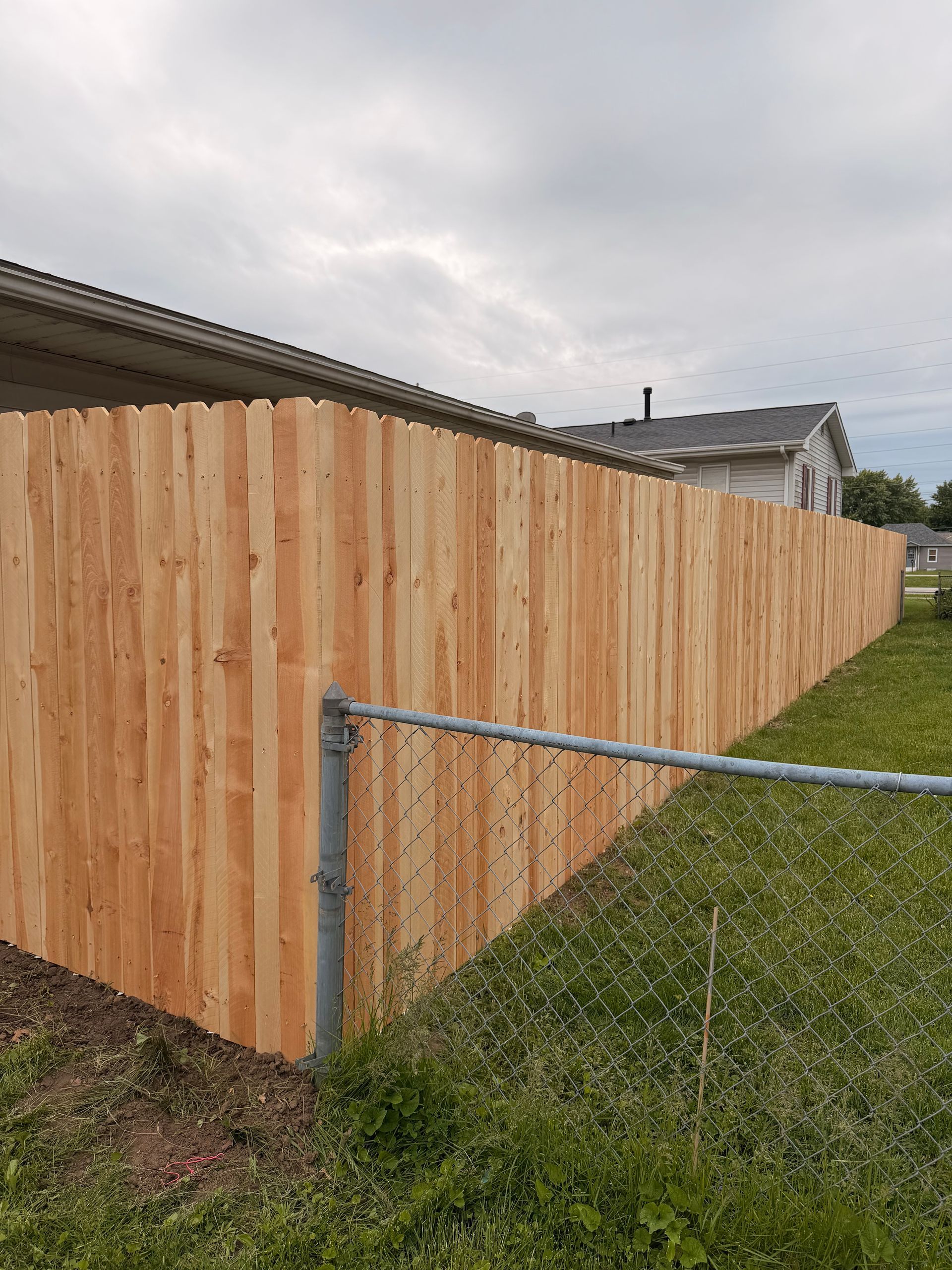 Wooden privacy fence along a grassy yard beside a chain-link gate under a cloudy sky