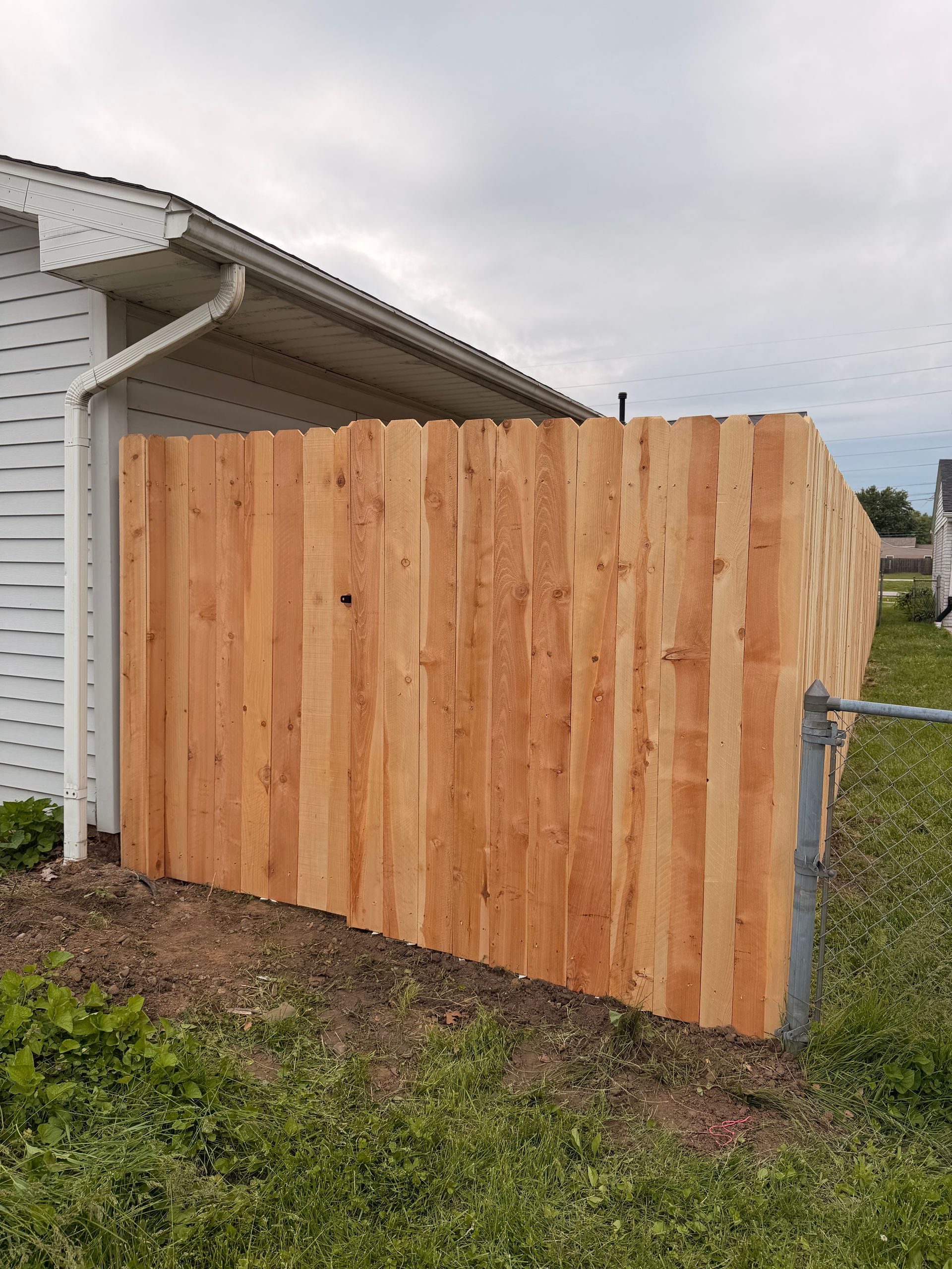 Freshly installed cedar fence panel beside a white house under a cloudy sky.
