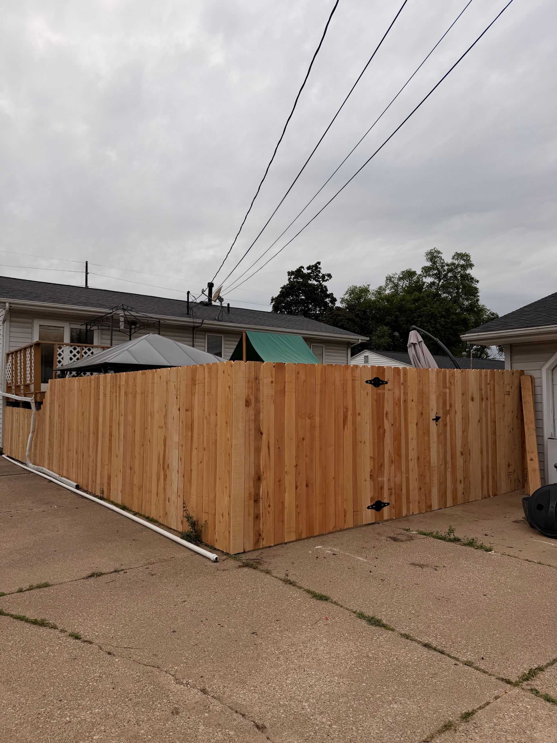 Wooden fenced enclosure on a driveway in front of a house under overcast skies