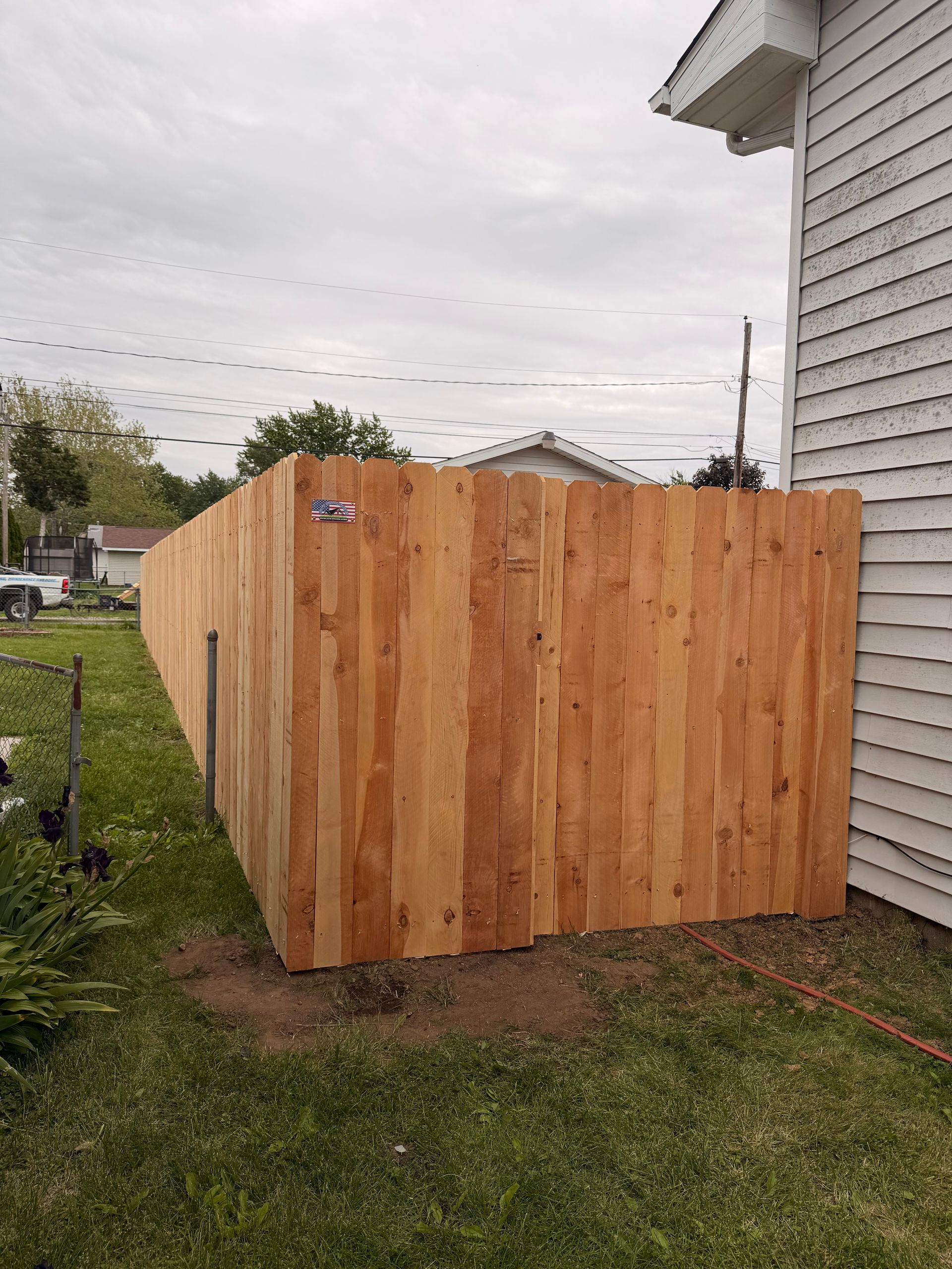Wooden privacy fence enclosing a small yard beside a white house.