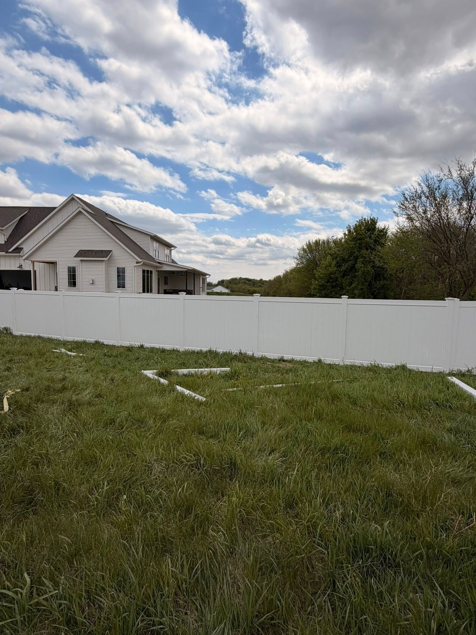 Suburban house behind a white fence, with green lawn and cloudy sky.