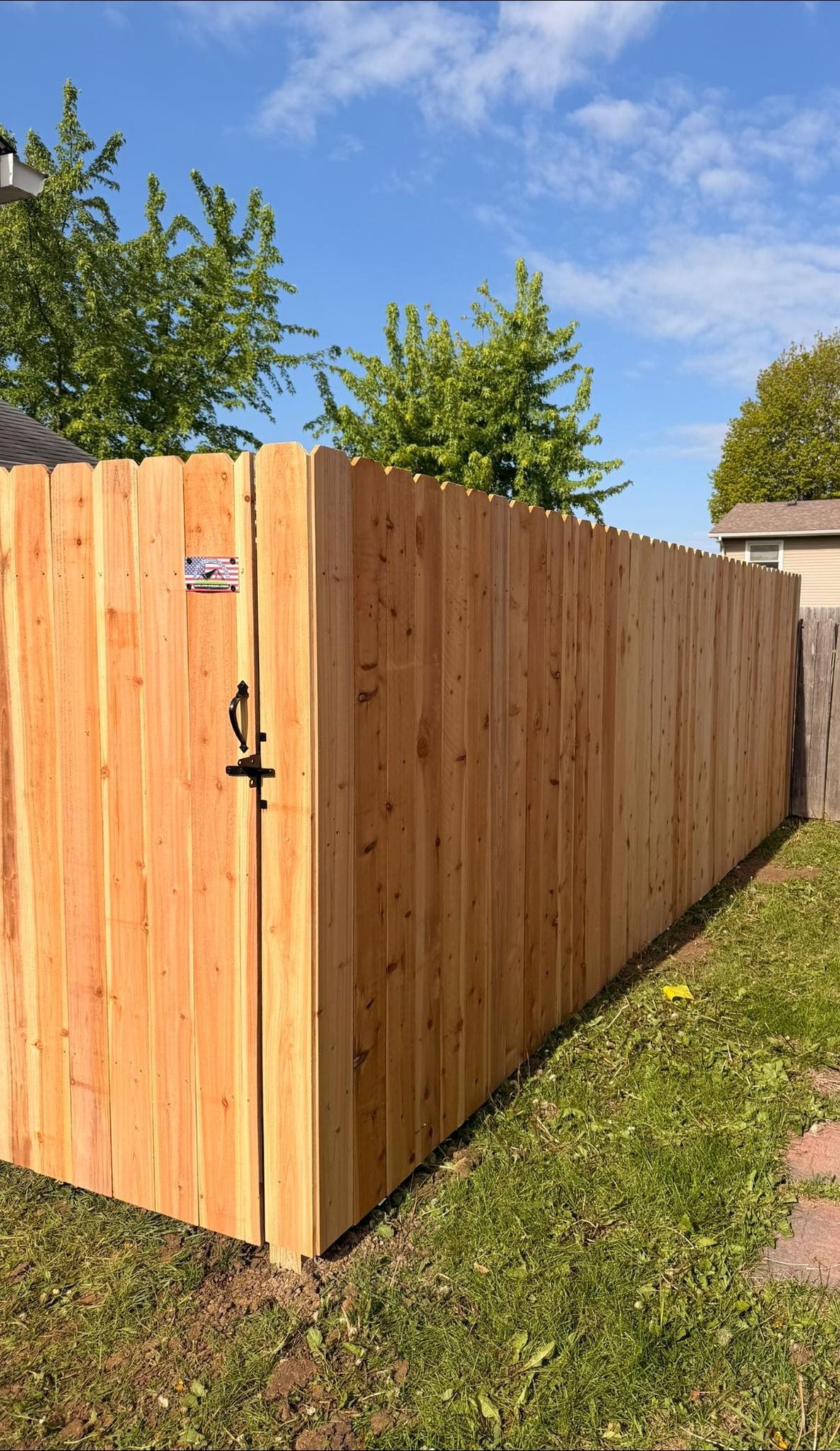 Wooden privacy fence with a gate beside a grassy yard under a blue sky.