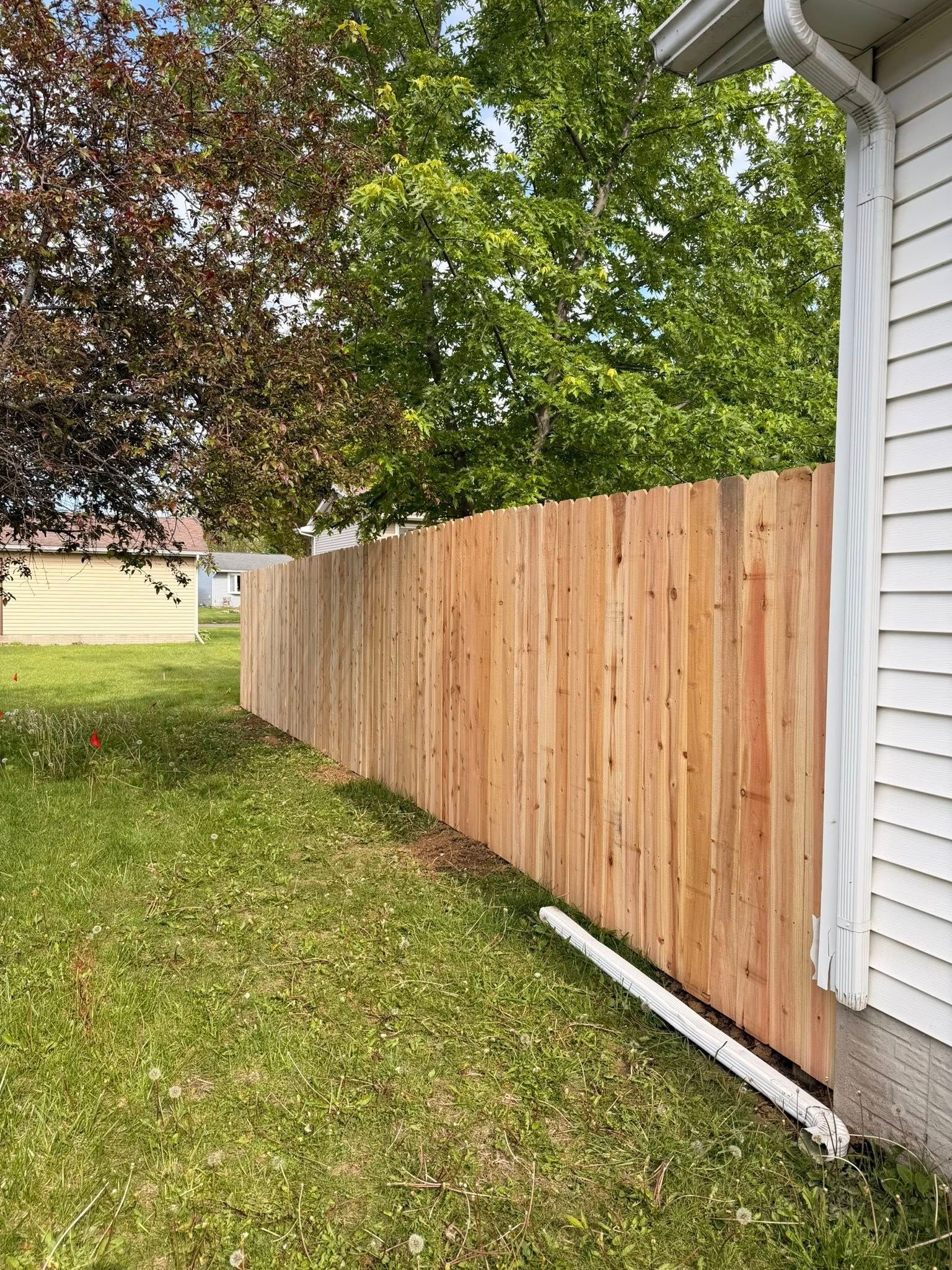 Wooden privacy fence beside a white house in a grassy yard with trees overhead