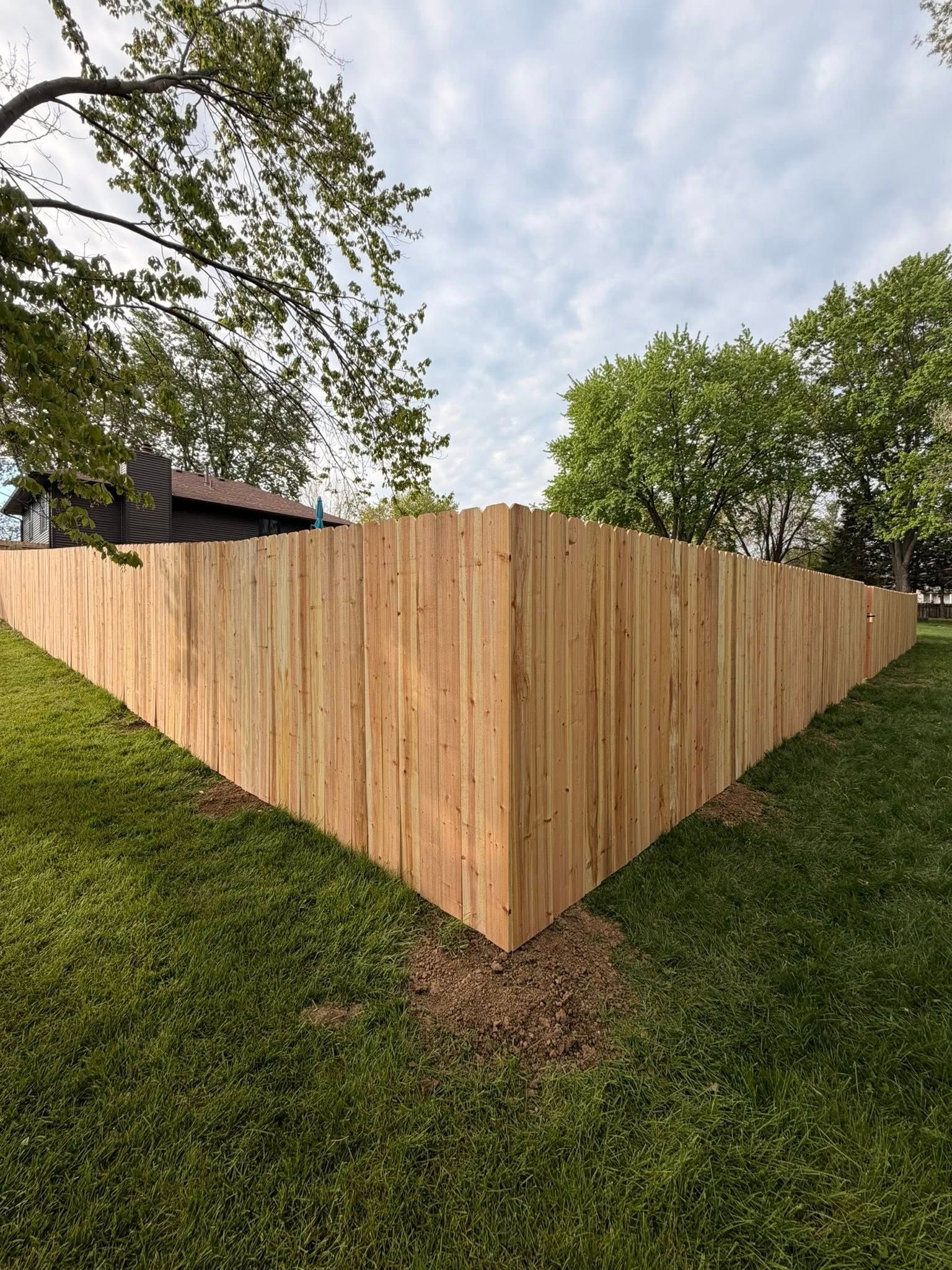 Wooden corner fence enclosing a sloped grassy yard under a cloudy sky