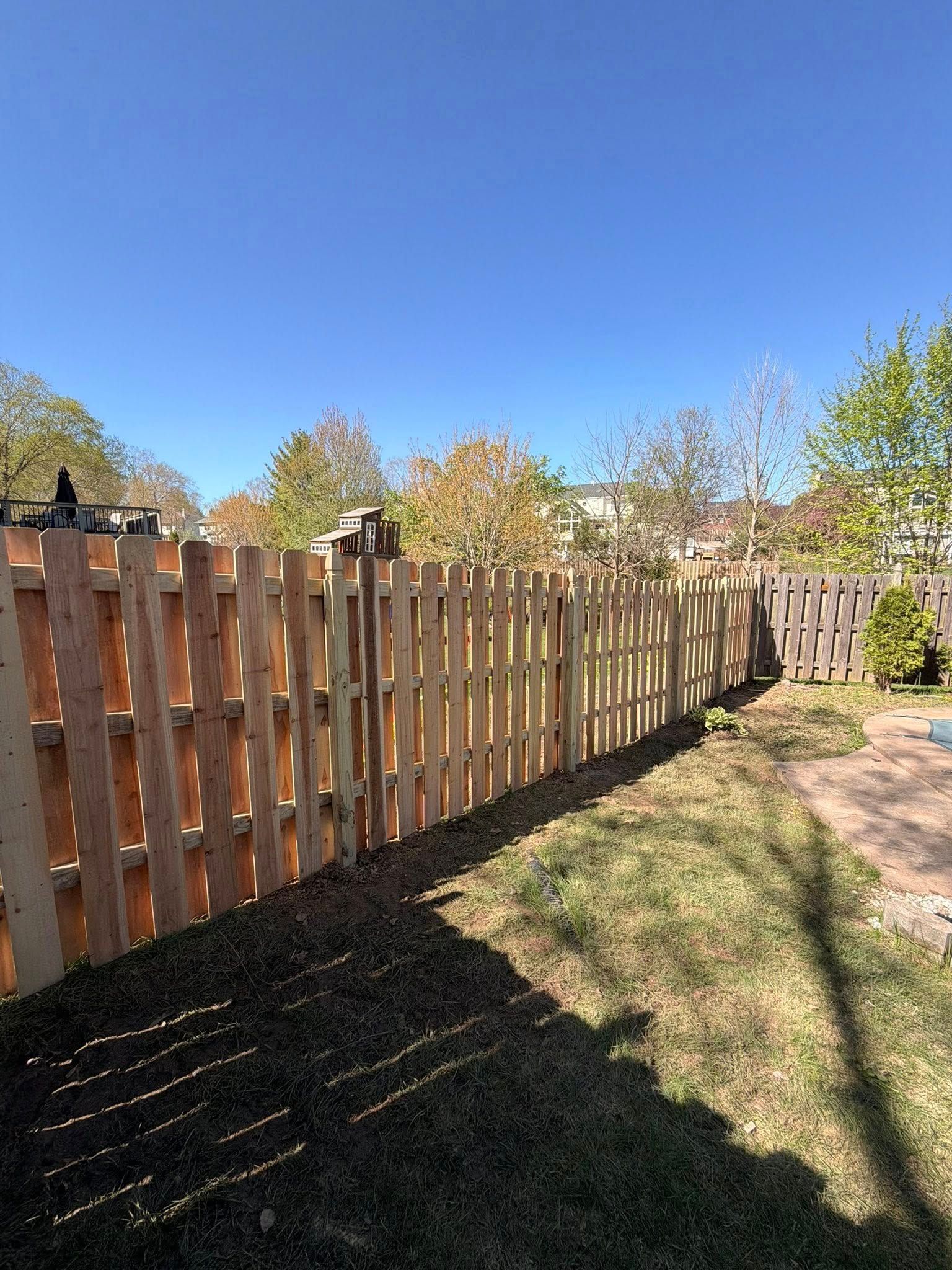 Wooden fence along a grassy yard under a clear blue sky on a sunny day