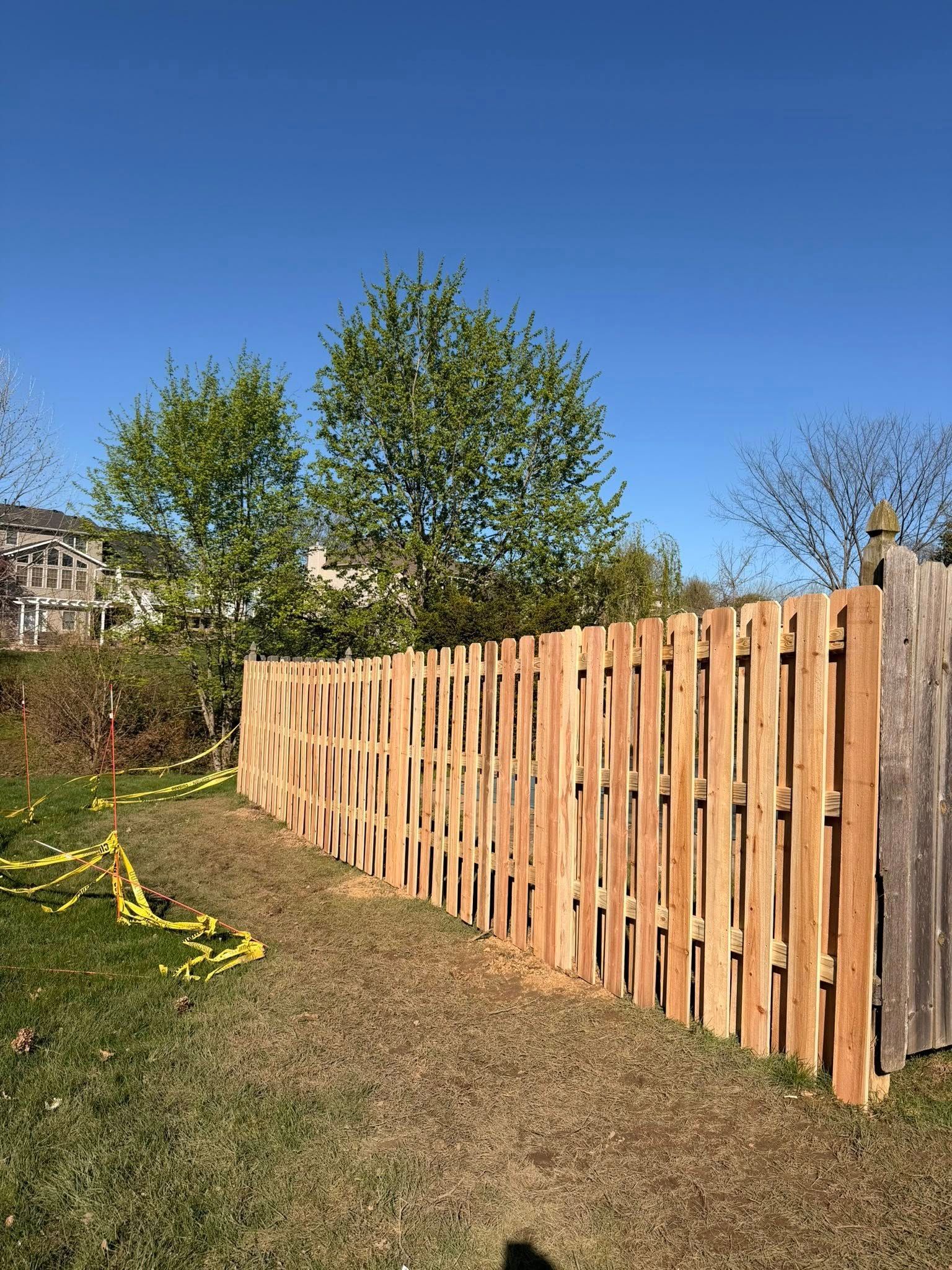 Wooden fence beside a grassy yard under a clear blue sky, with trees in the background.