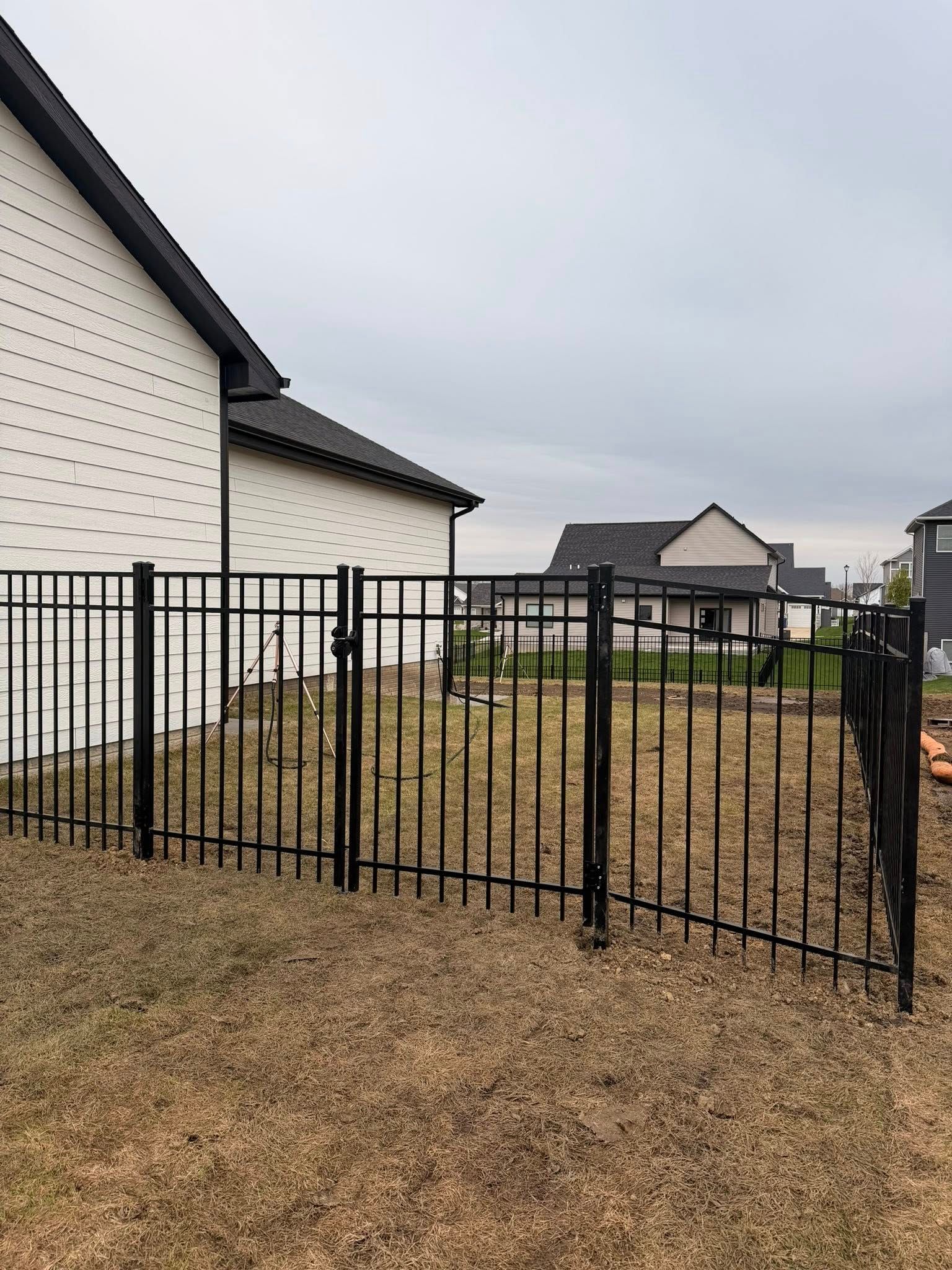 Black metal fence in front of a beige house and gravel yard under an overcast sky