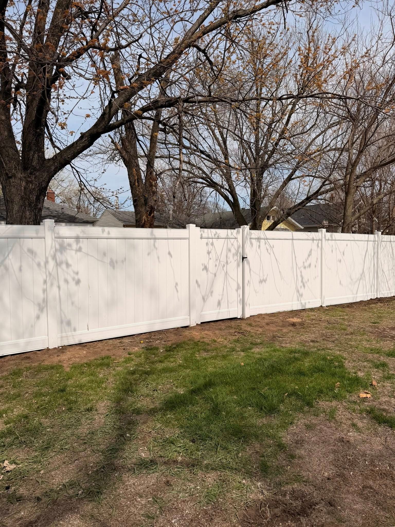 White fence along a grassy yard with leafless trees in the background