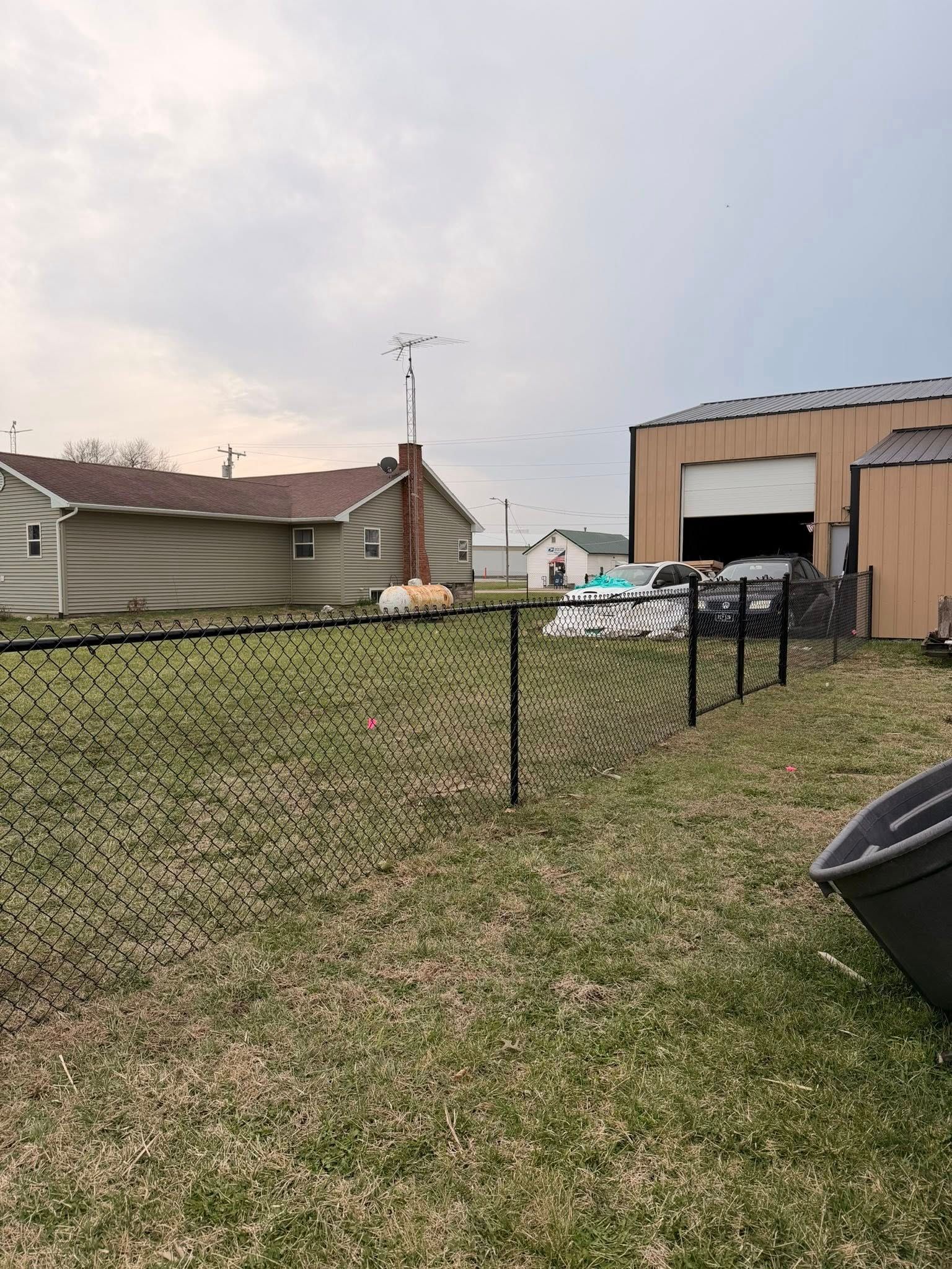 Backyard with chain-link fence, grassy yard, house, and large shed under cloudy sky