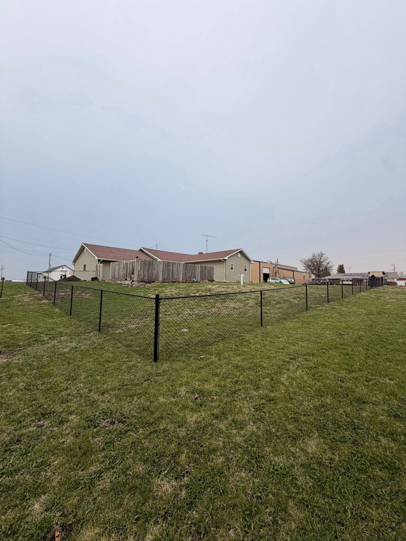 Rural field with fence posts and a row of houses under a cloudy sky
