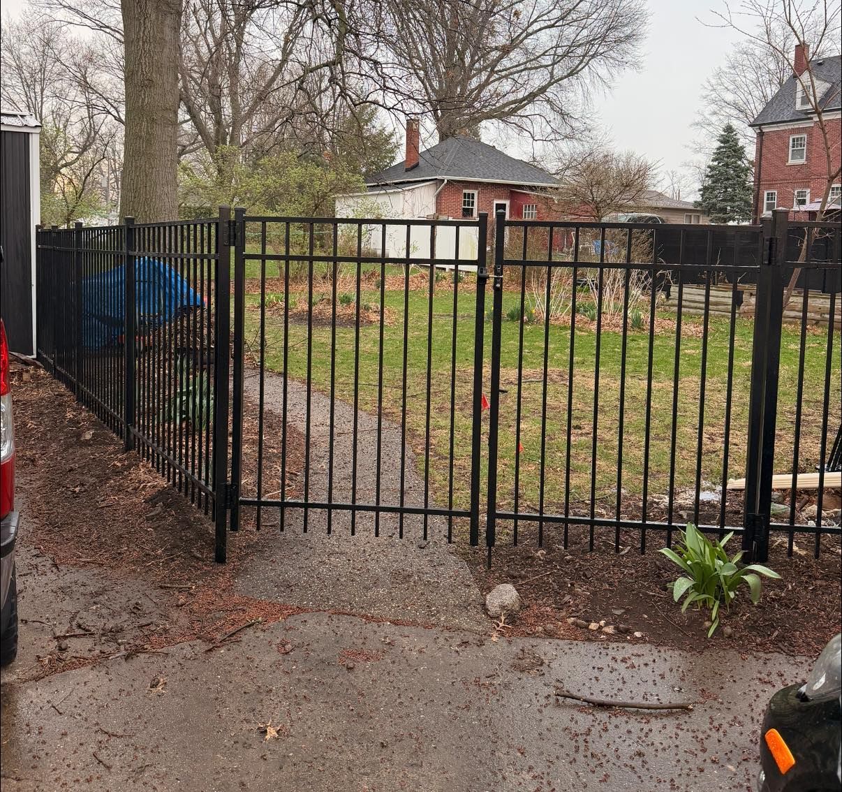 Black metal fence across a small yard with leafless trees and houses in the background