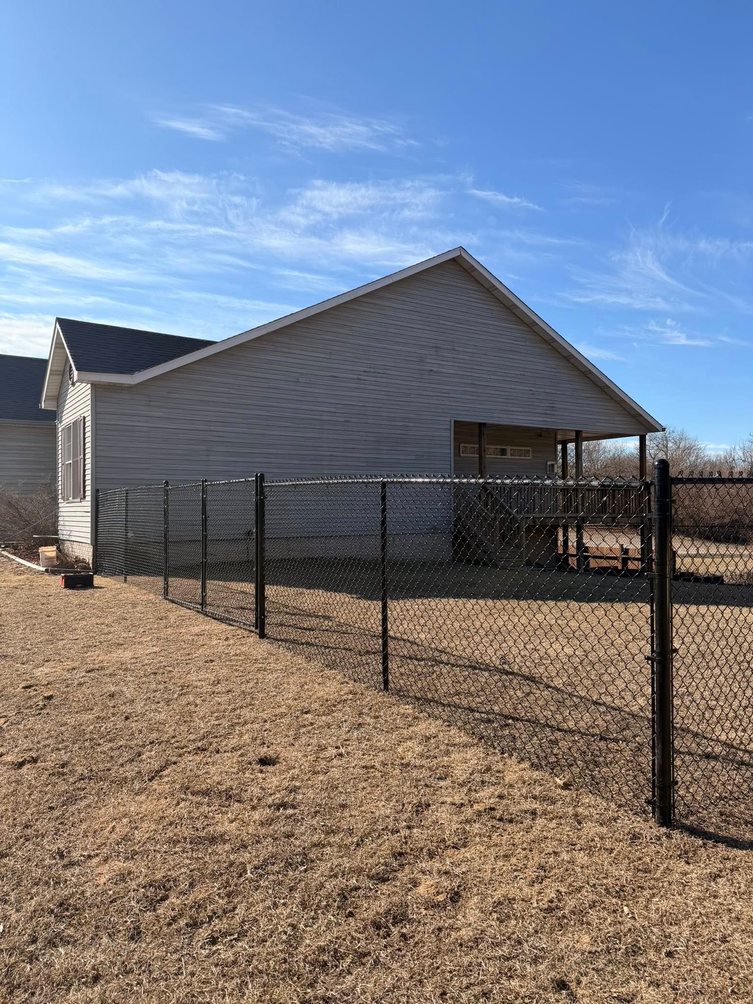 Black metal fence in front of a beige house under a blue sky on a gravel lot