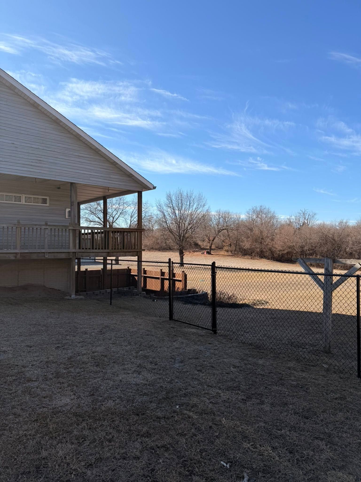 Backyard beside a beige house with a black fence, leafless trees, and a bright blue sky