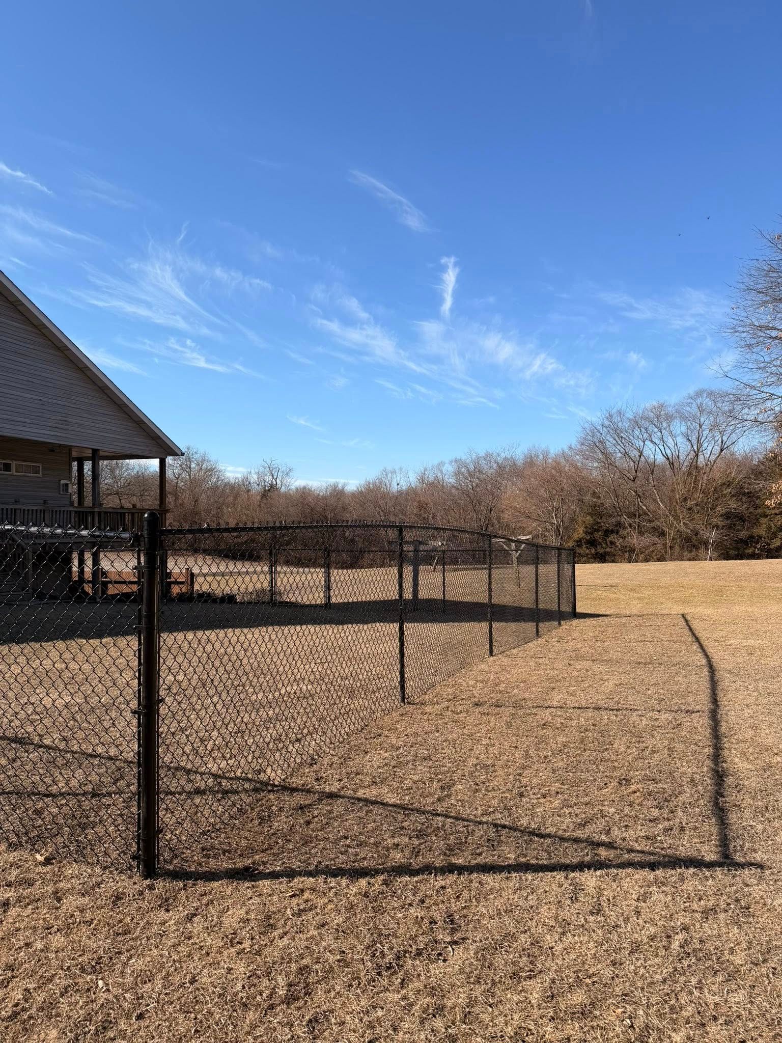 Black metal fence enclosing a gravel yard beside a house under a clear blue sky