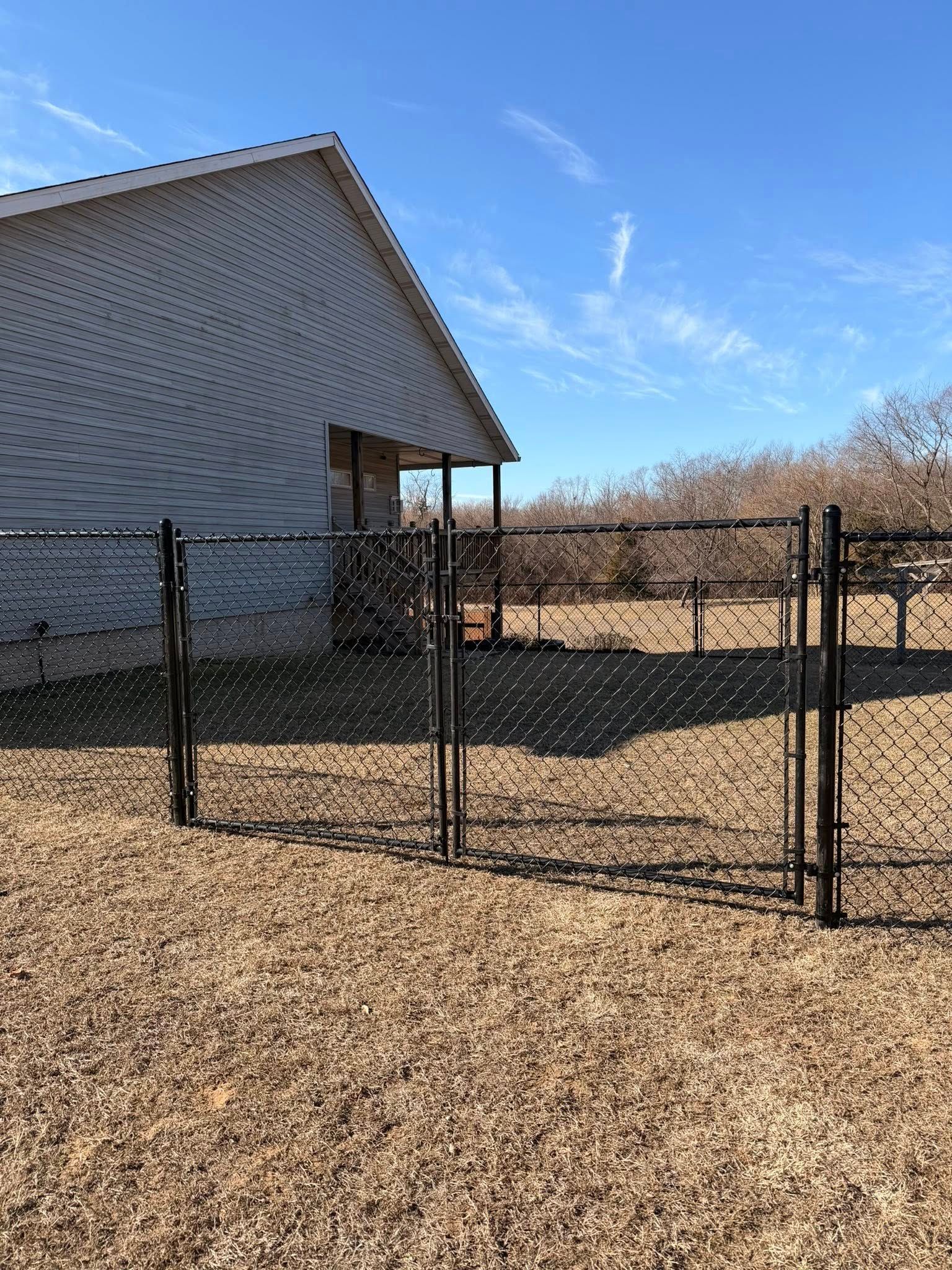 Black chain-link fence beside a tan building and gravel yard under a blue sky