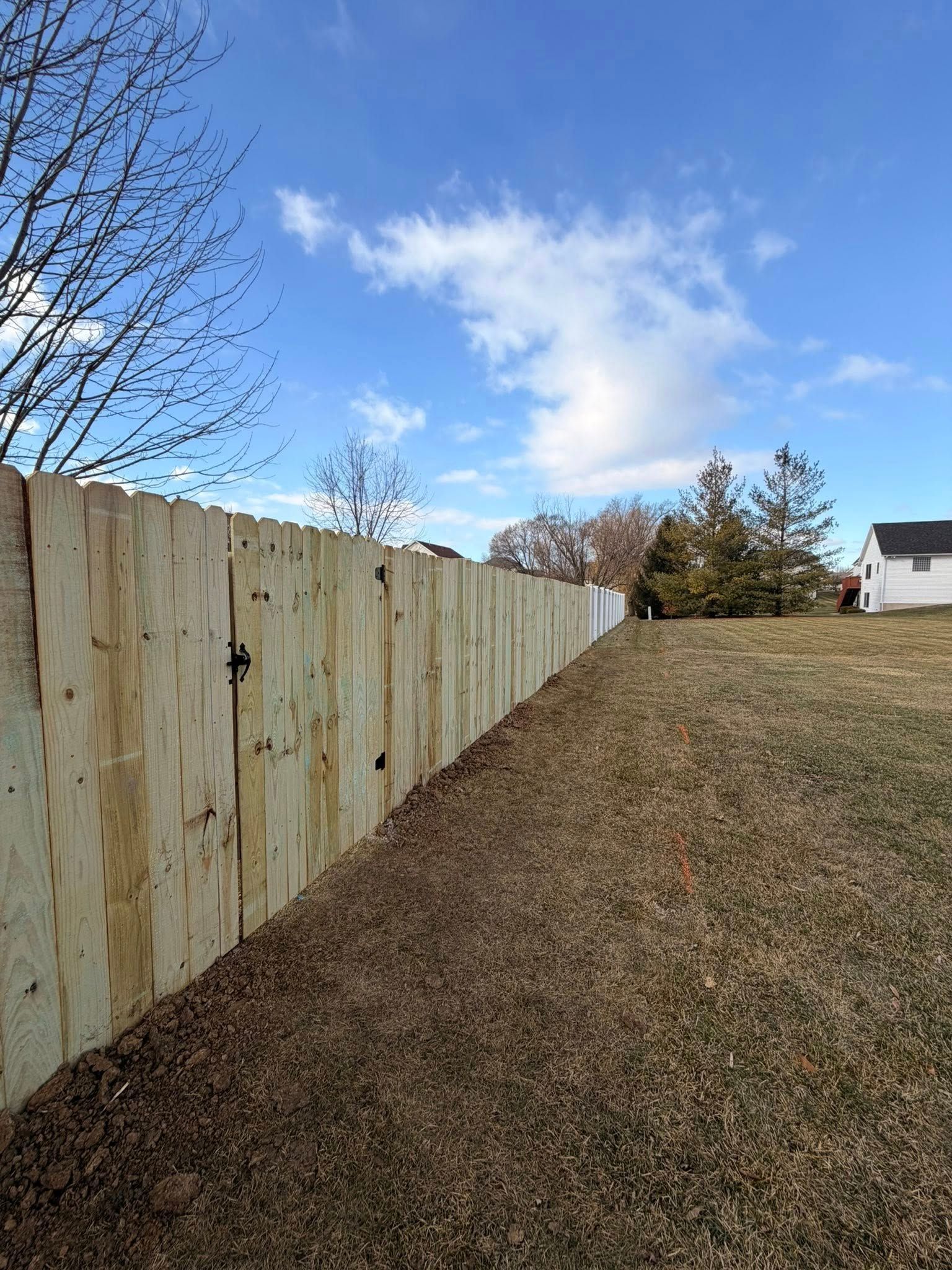 Wooden fence beside a sloping brown lawn under a blue sky with clouds