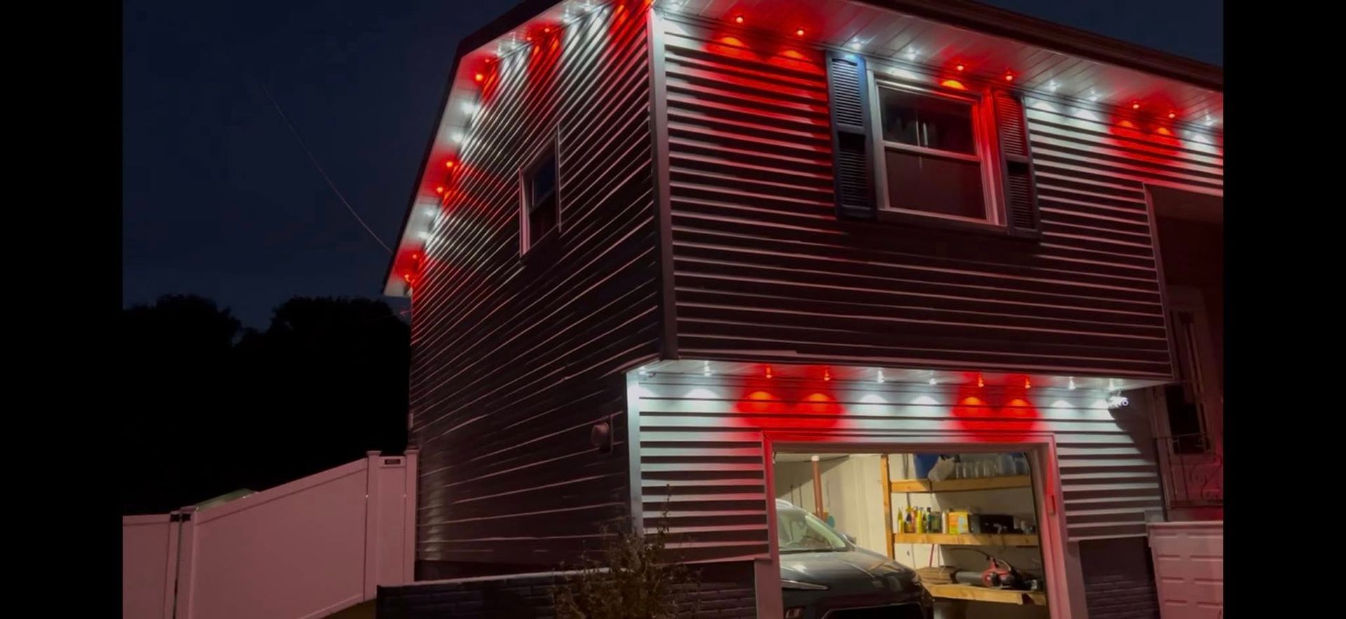 Two-story house at night with red holiday lights and an open garage.