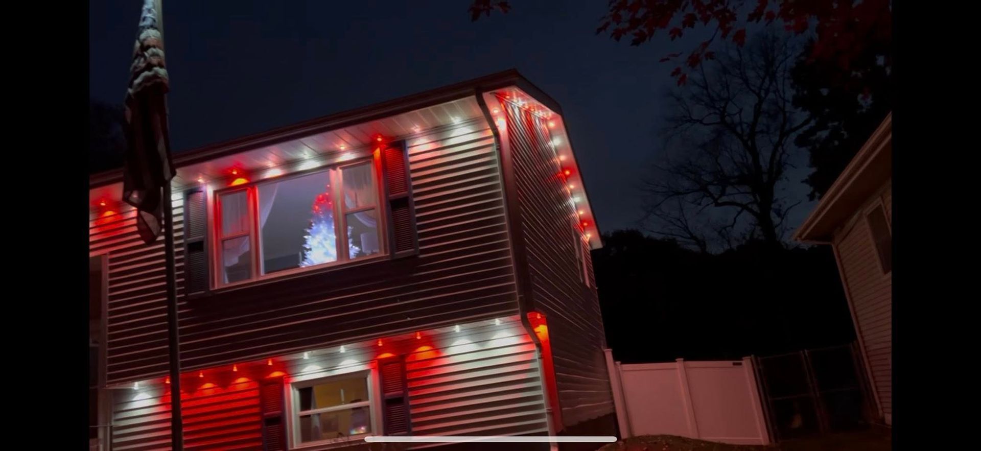 House decorated with red Christmas lights at night, with lit windows and a dark sky
