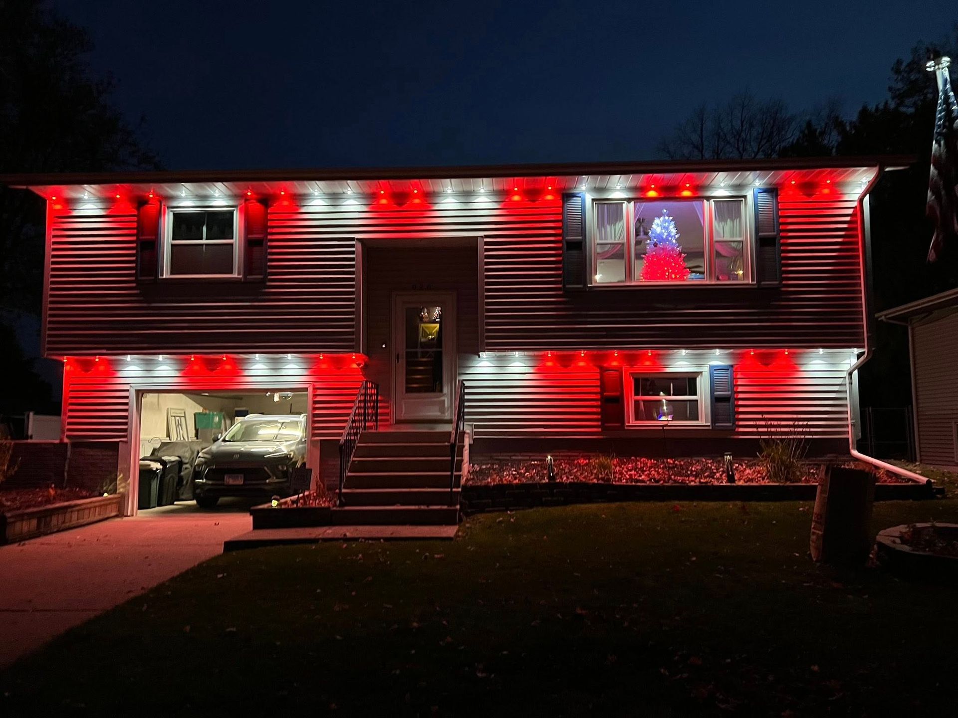 House at night with red holiday lights, illuminated windows, and an open garage.
