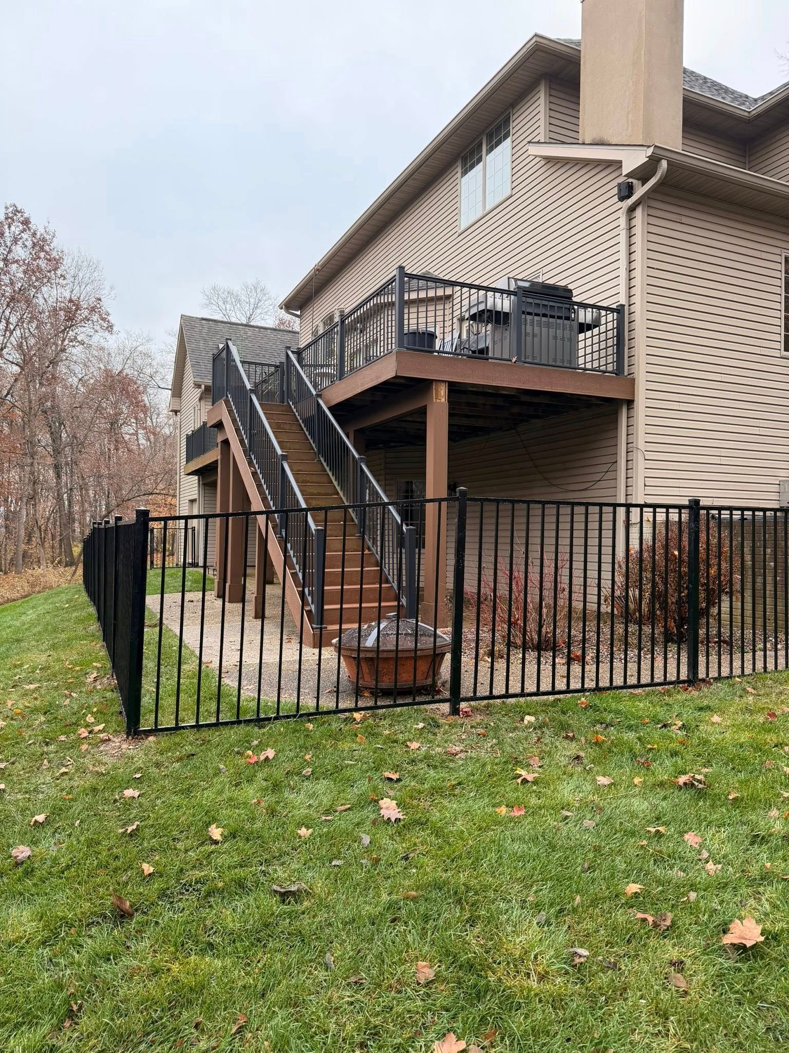 Apartment exterior with black metal staircase, balcony, and fenced grassy yard in autumn