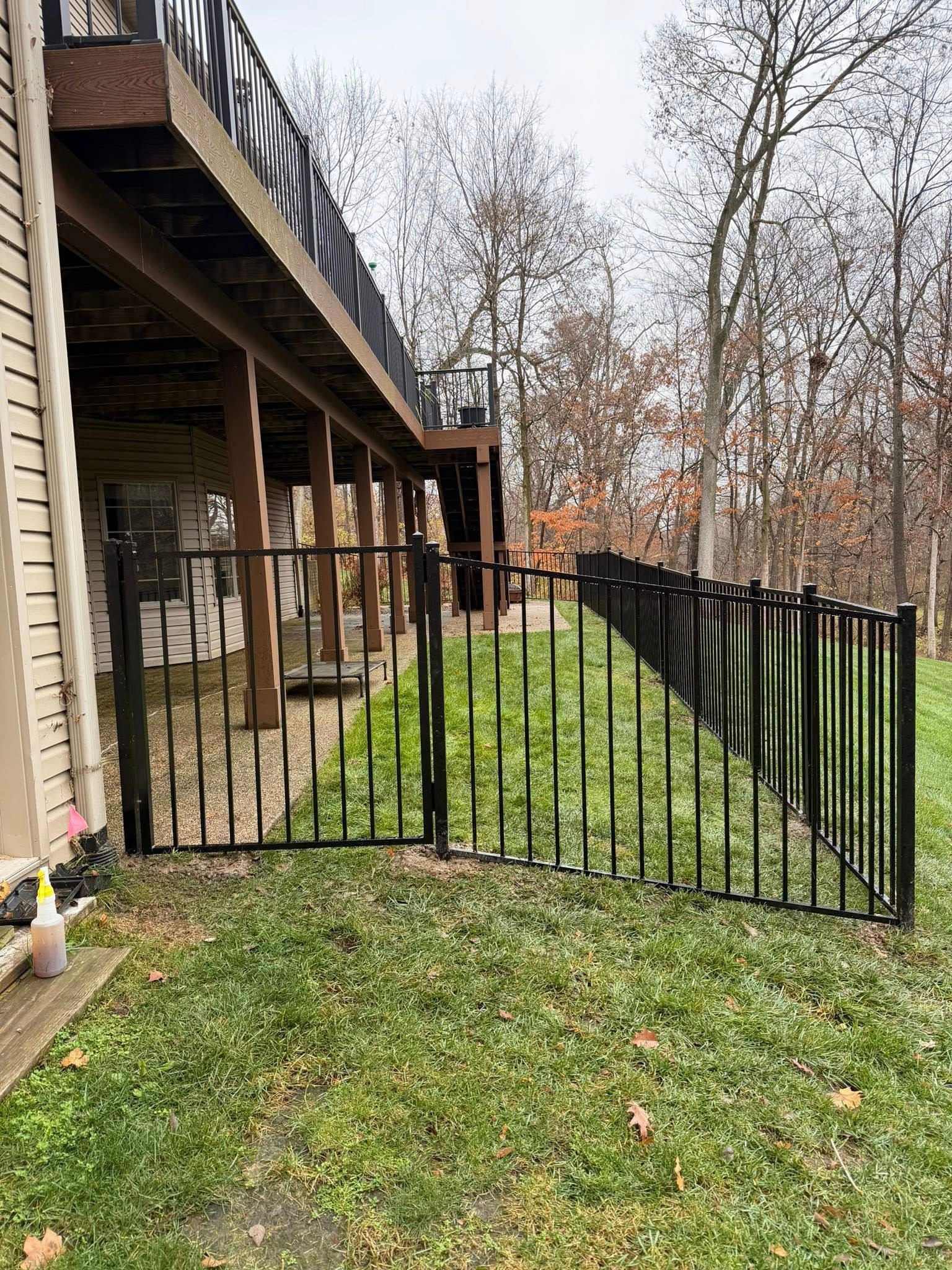 Black metal fence leaning along a house deck beside a grassy yard and leafless trees