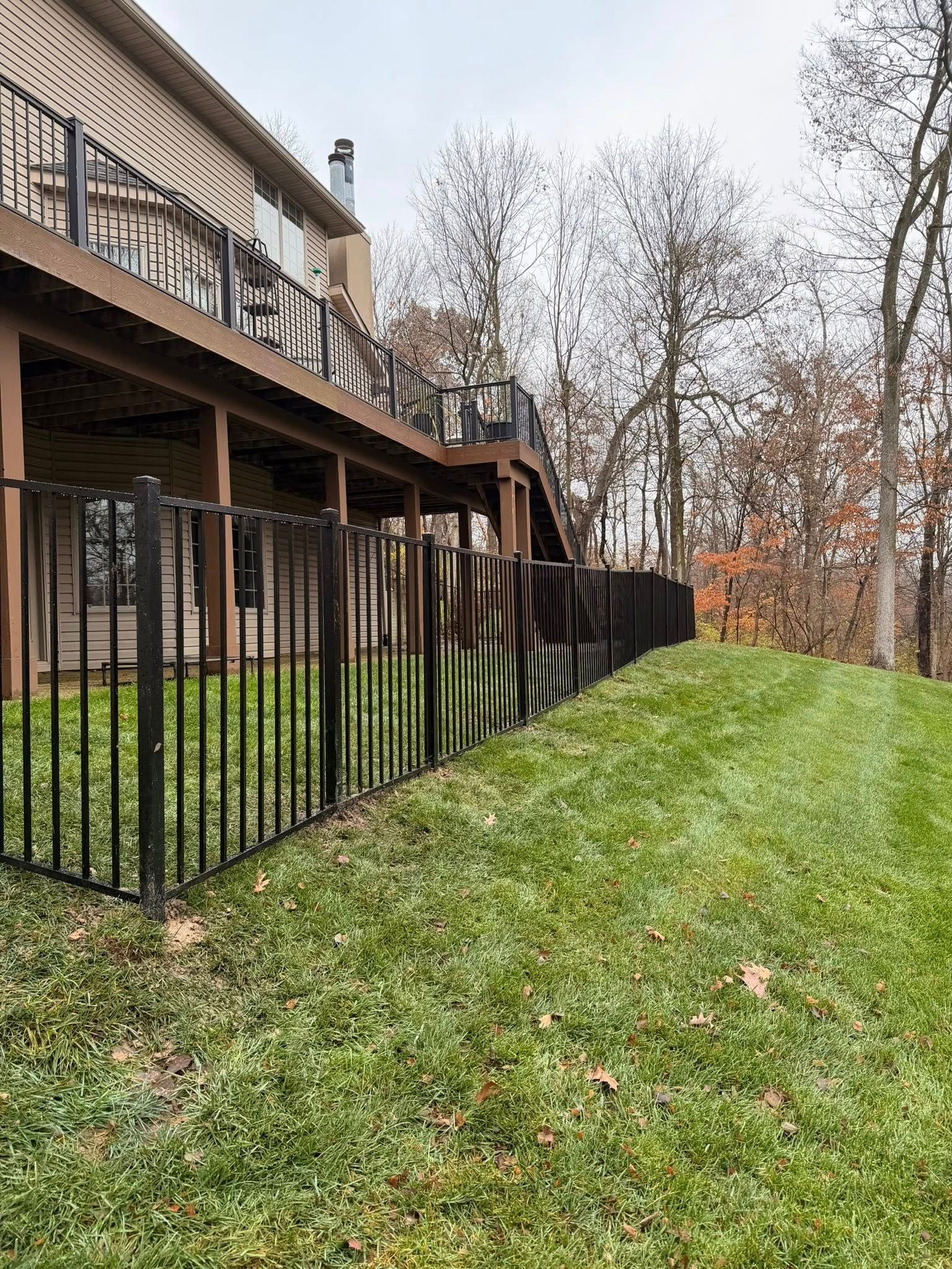 Backyard deck with black railing beside a grassy slope and leafless trees in fall.