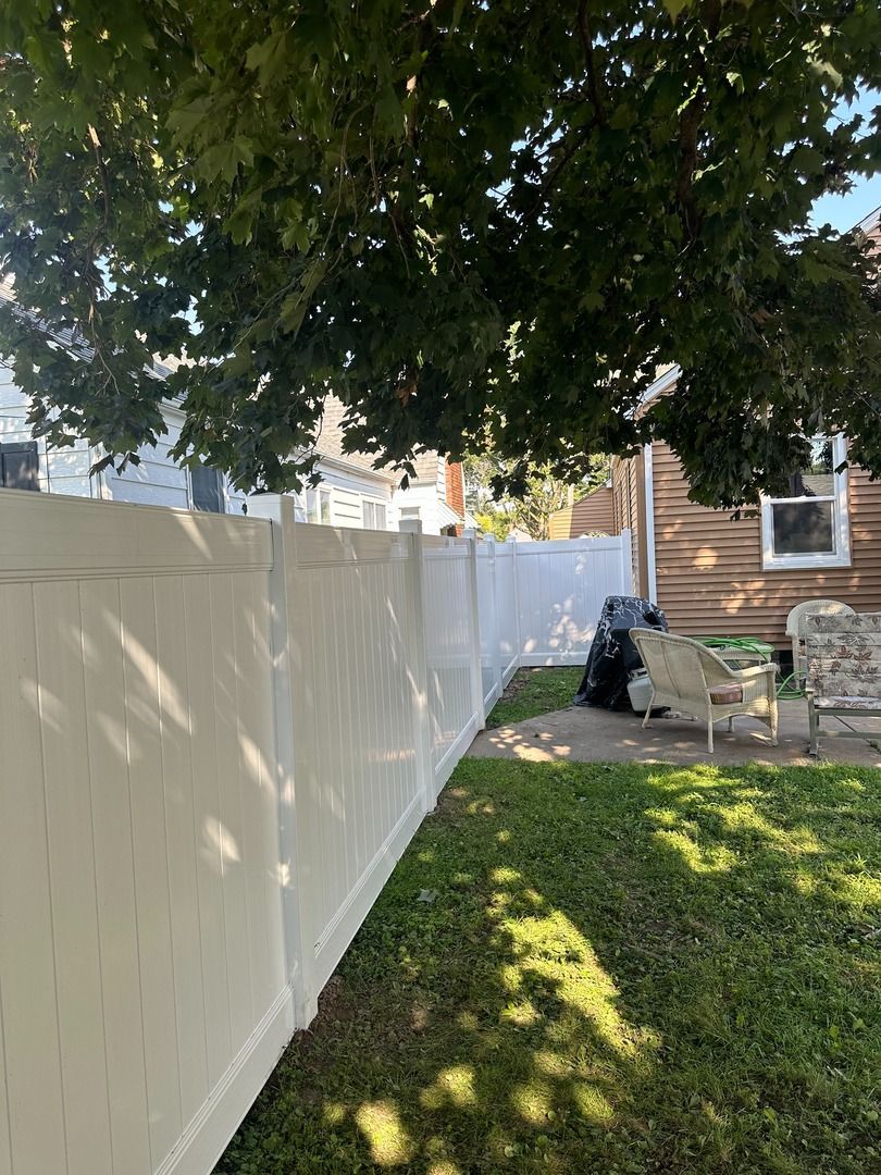 Backyard with white fence, tree shade, grass, and a house with patio furniture