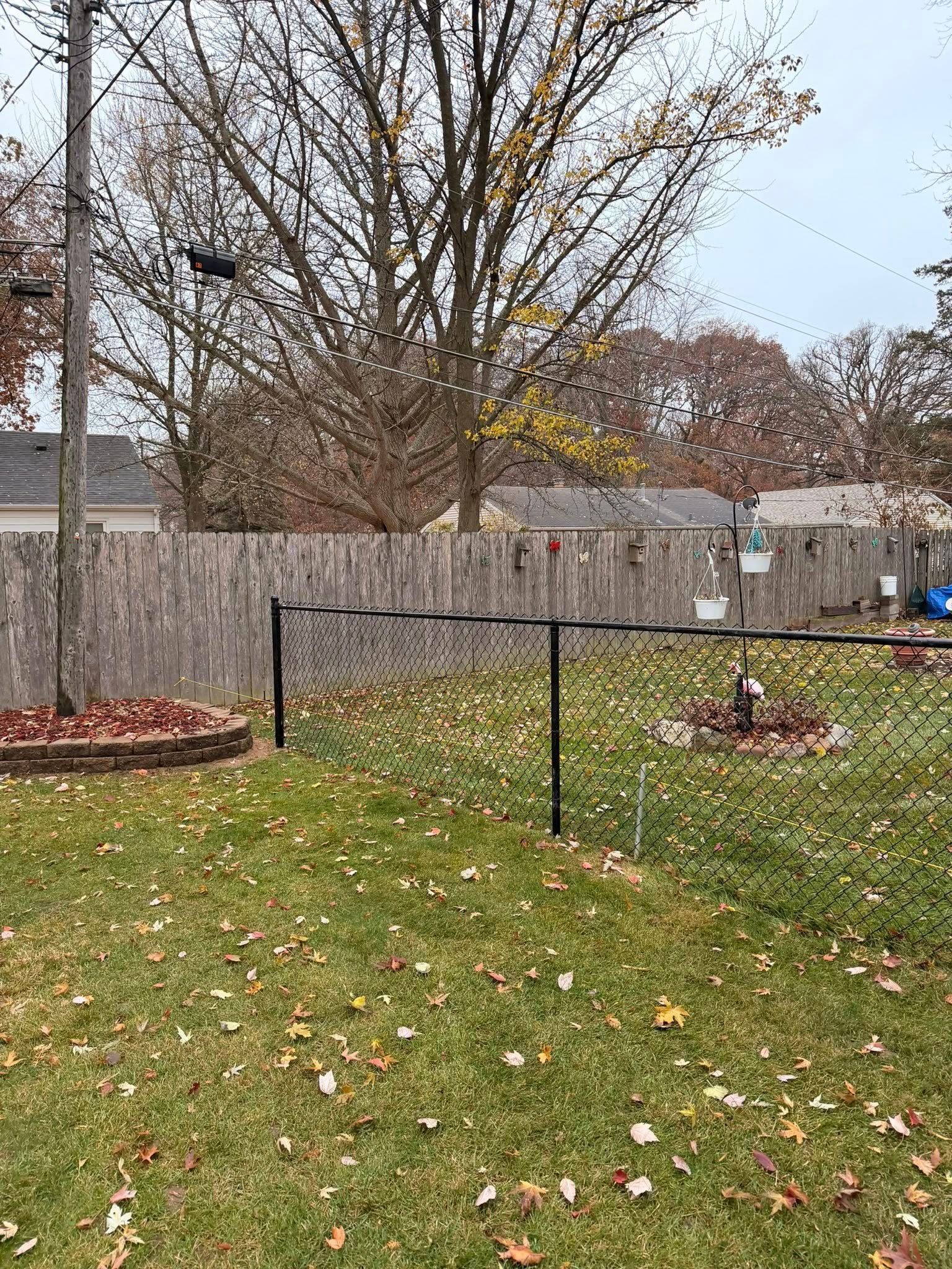 Backyard with fallen leaves, black metal fence, and flower beds under bare trees in autumn