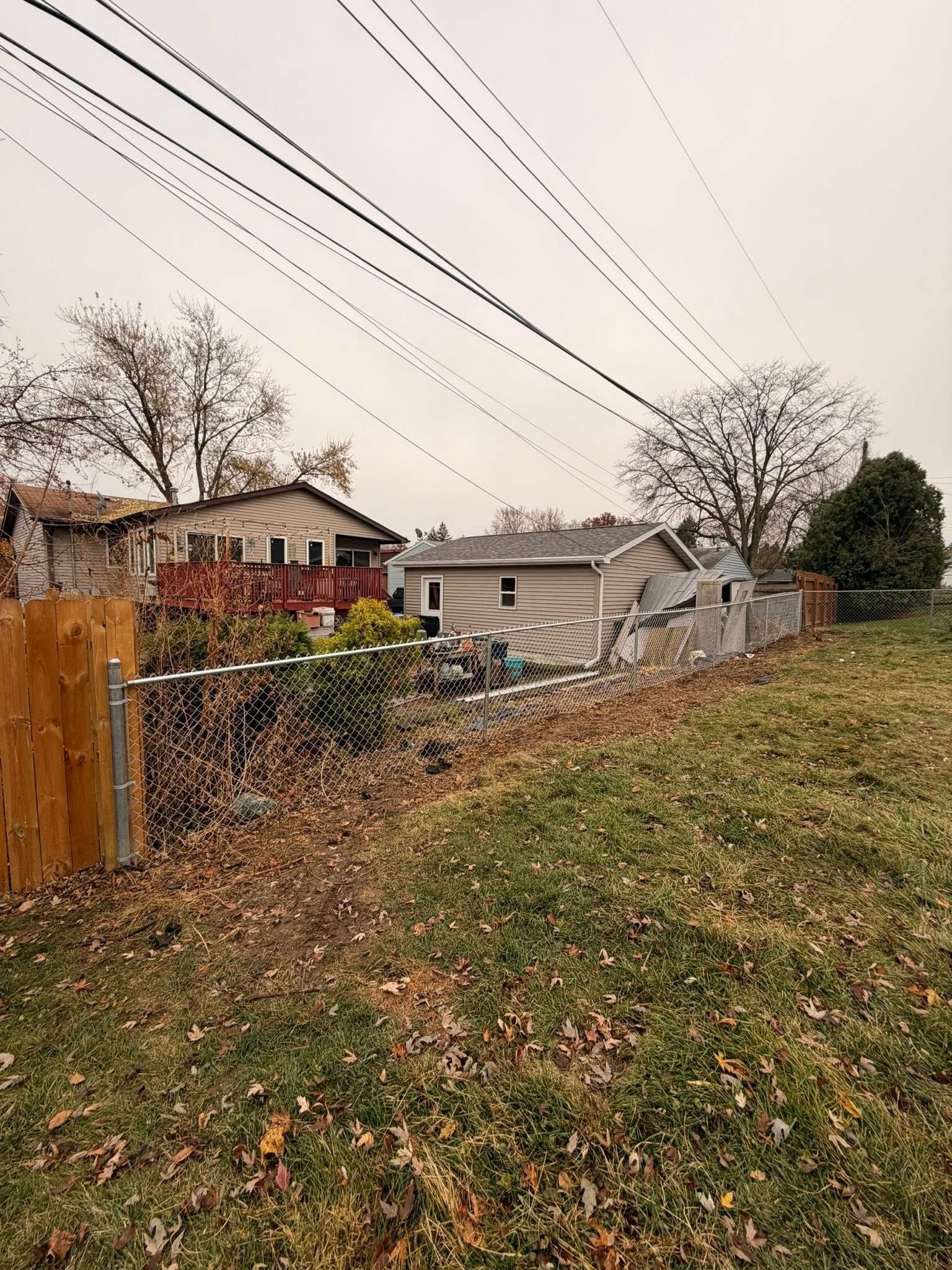 Suburban backyard with chain-link fence, fallen leaves, and houses under overcast skies
