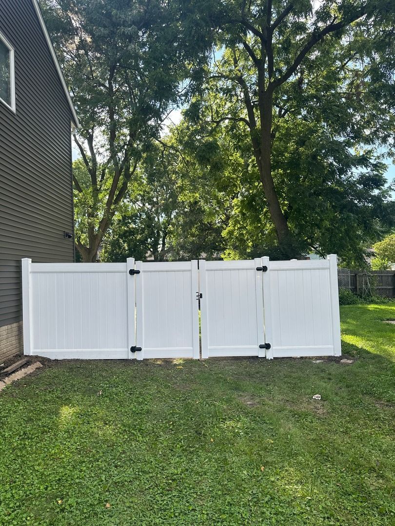 White folding fence panels leaning on a grassy yard beside a house and trees.
