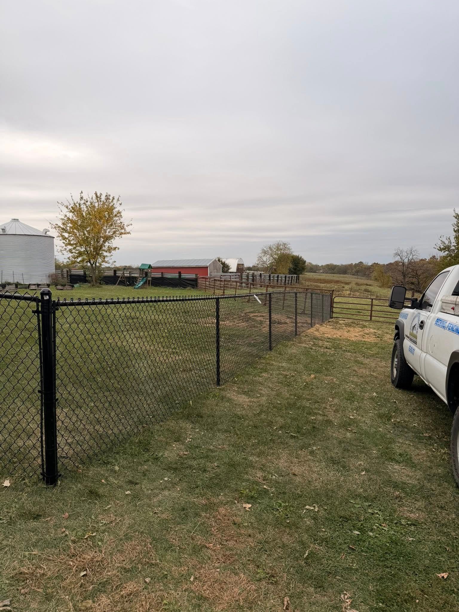 Chain-link fence along a grassy yard with a white truck parked beside it under an overcast sky.