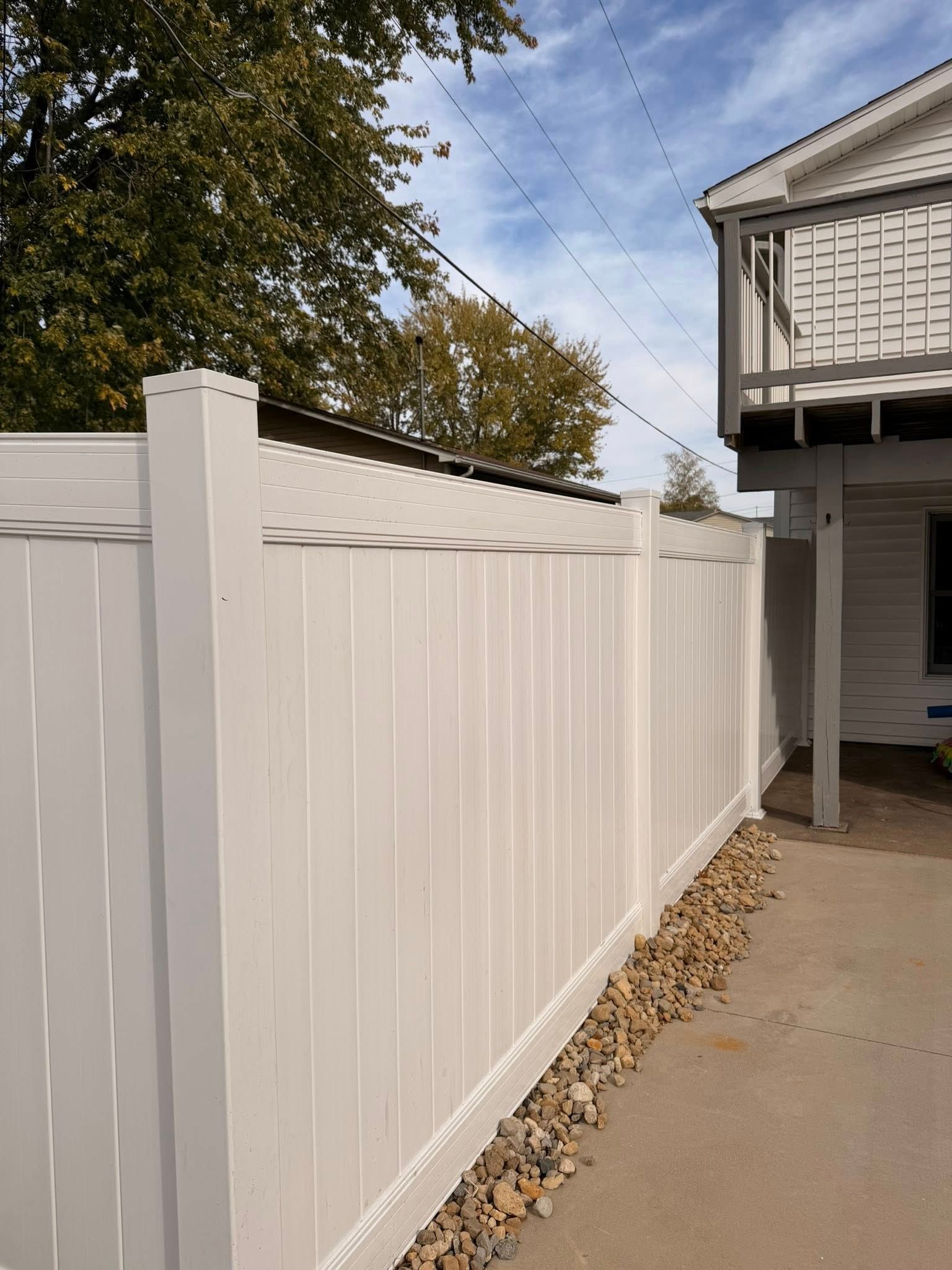 White vinyl privacy fence along a concrete driveway beside a house and fallen leaves