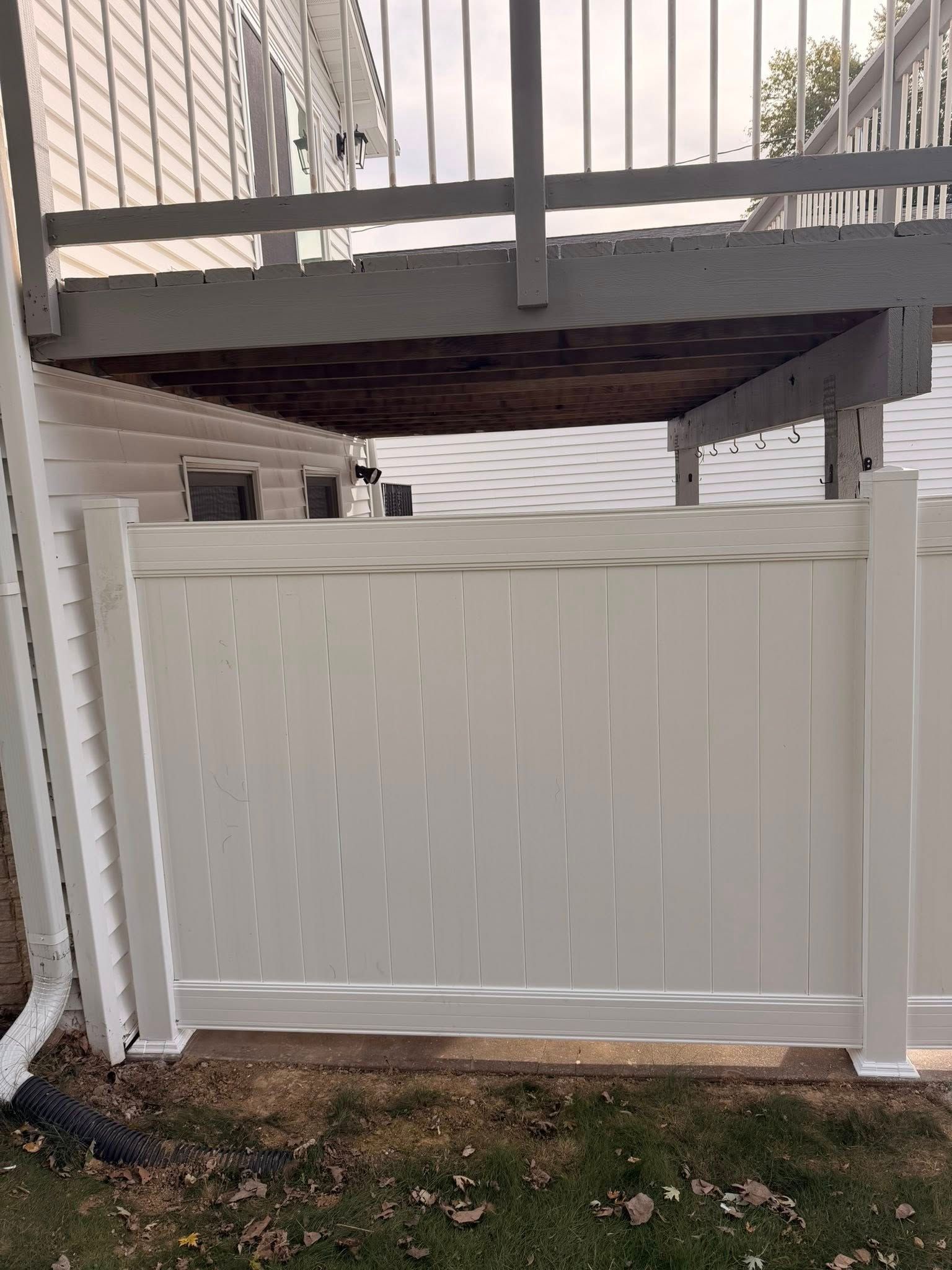 White vinyl fence and gate beneath an elevated deck in a small yard.