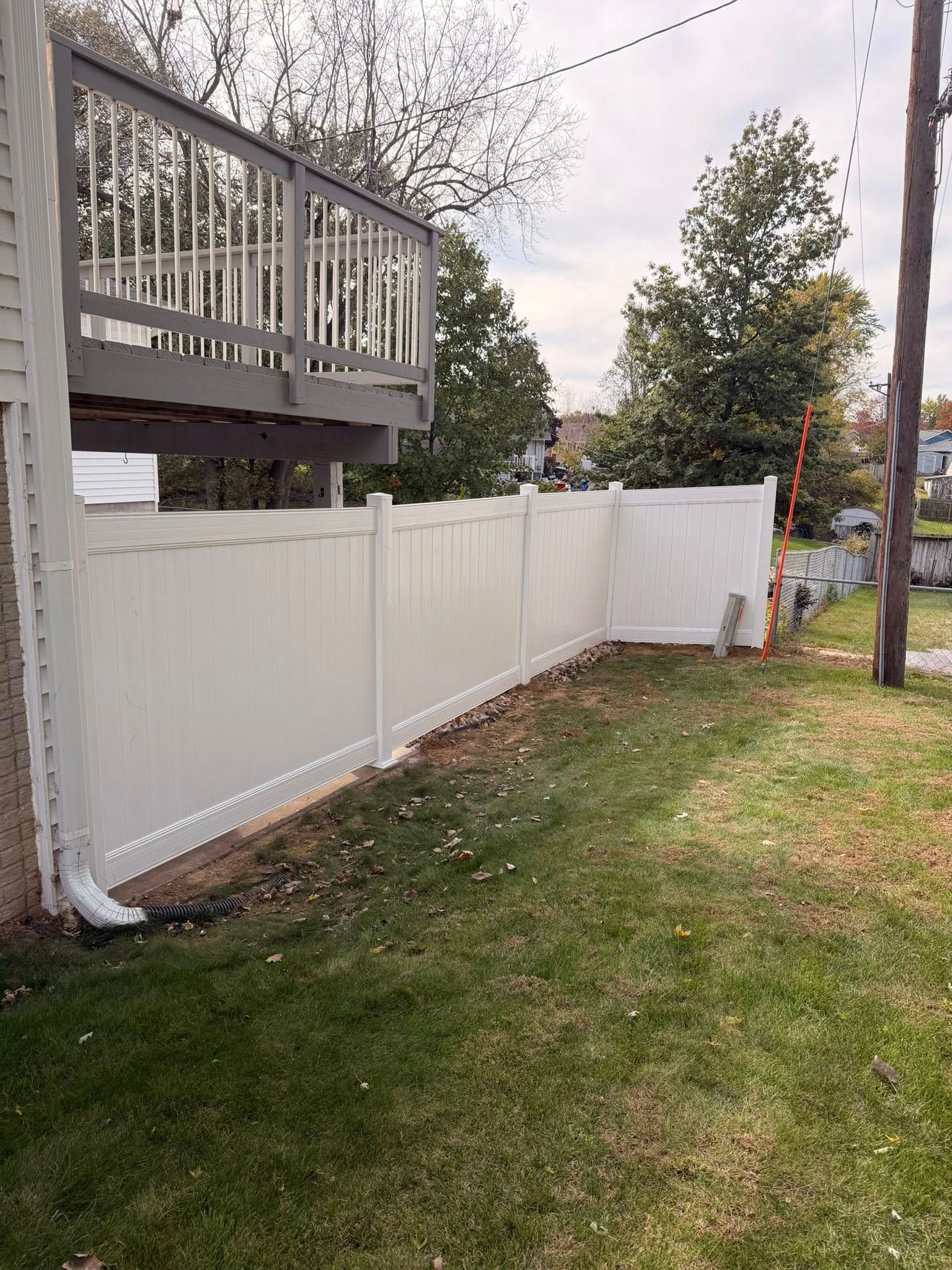 White vinyl fence beside a raised deck in a grassy yard with trees and a utility pole