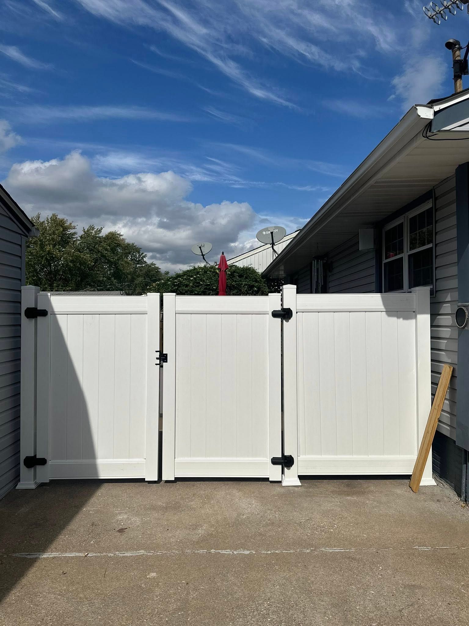White double gate with black hinges between two houses under a blue sky.