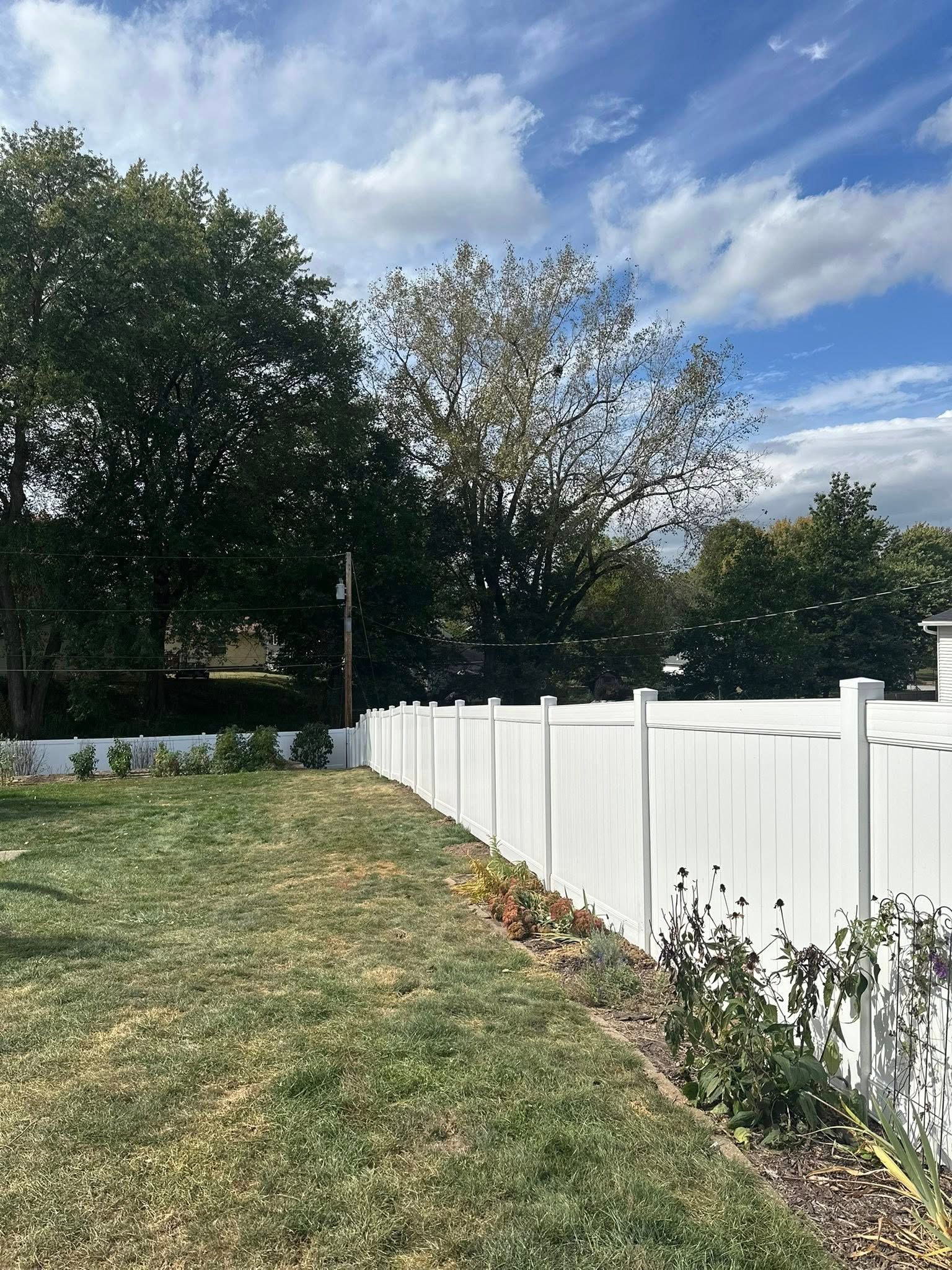 Backyard with green lawn, white fence, and trees under a partly cloudy sky