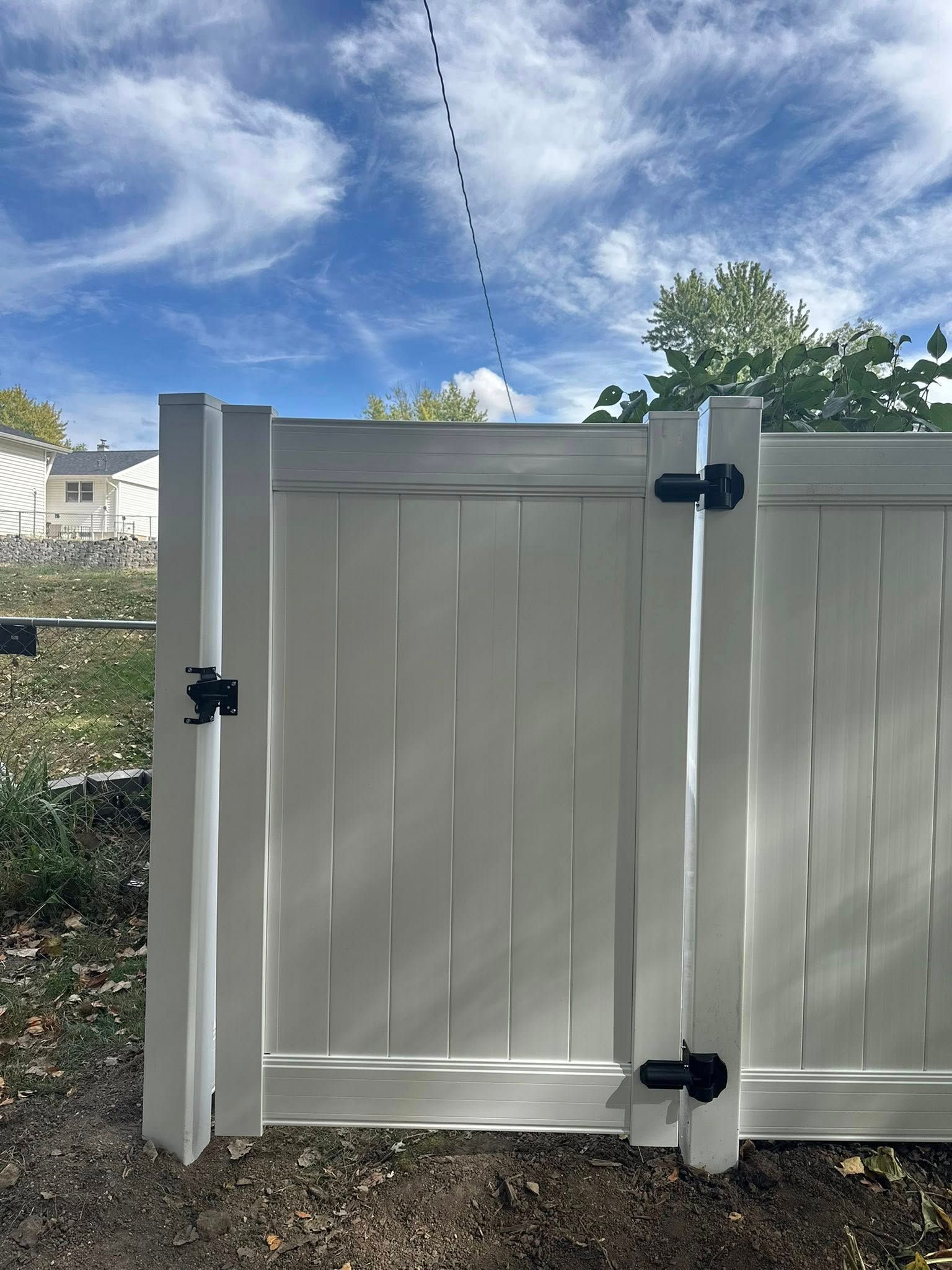 White vinyl fence gate with black hinges under a blue sky outdoors