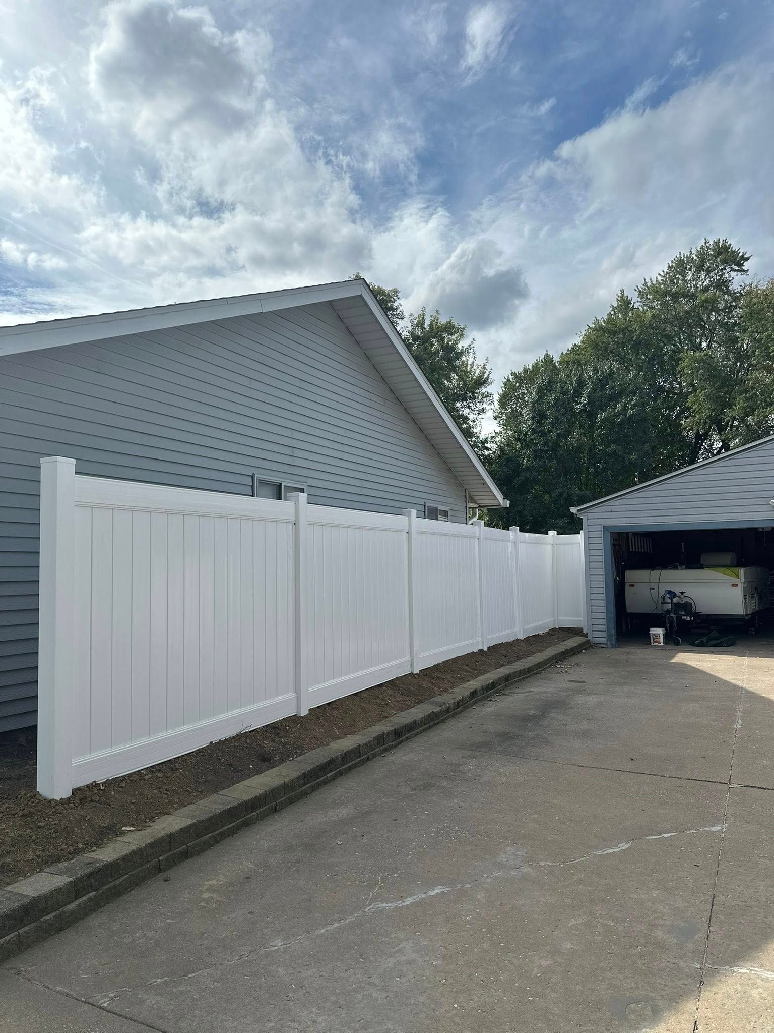 White vinyl fence beside a gray house and garage under a partly cloudy sky
