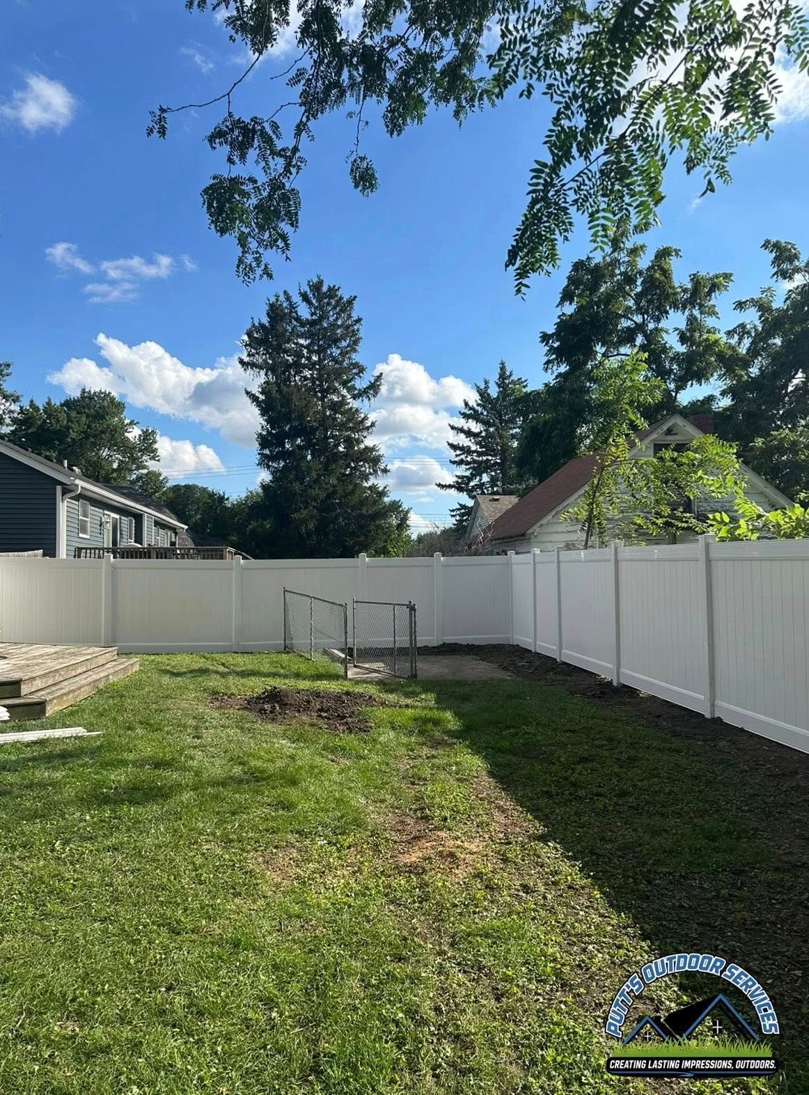 Backyard with green lawn, white fence, trees, and a sunny blue sky