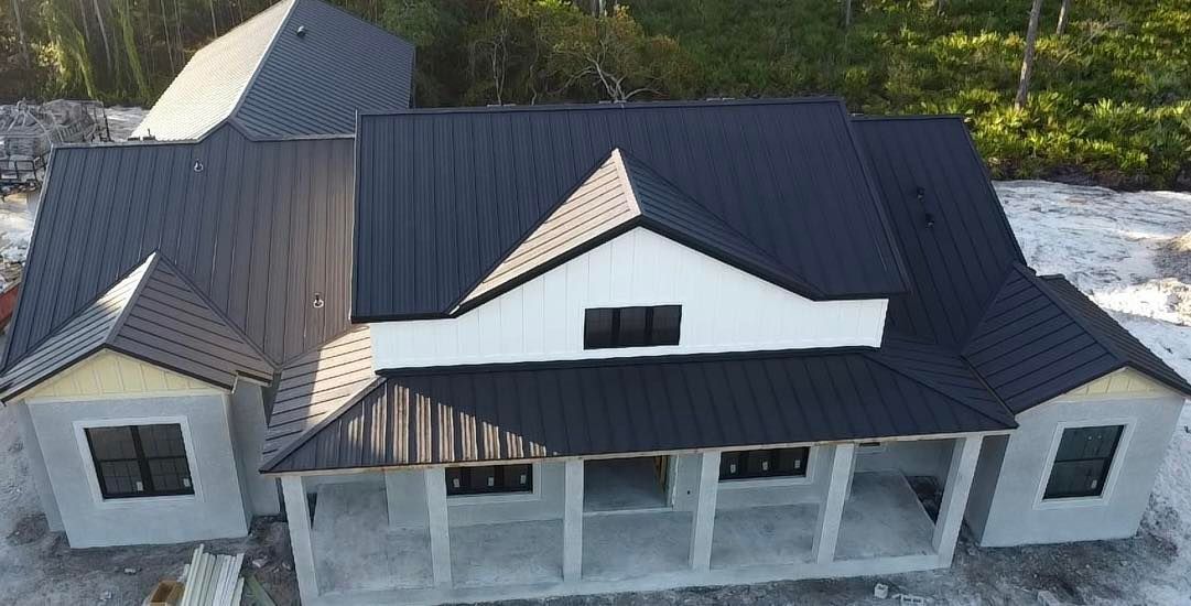 Aerial view of a newly built house with a dark roof and white exterior, surrounded by bare ground and trees.