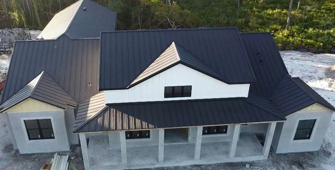 Aerial view of a newly built house with a dark roof and white exterior, surrounded by bare ground and trees.