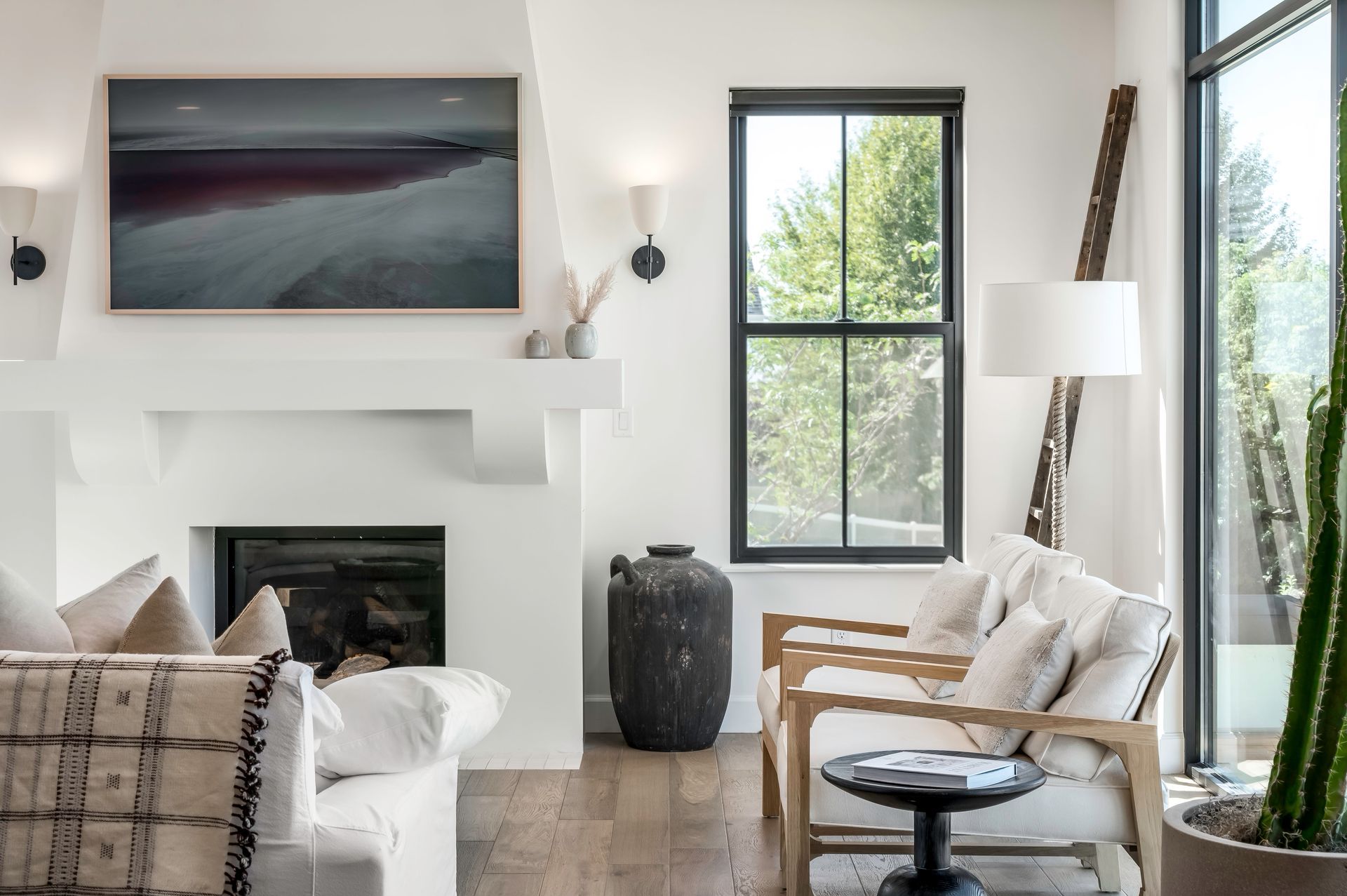 Bright living room with white fireplace, black-framed windows, and beige chairs by a glass door