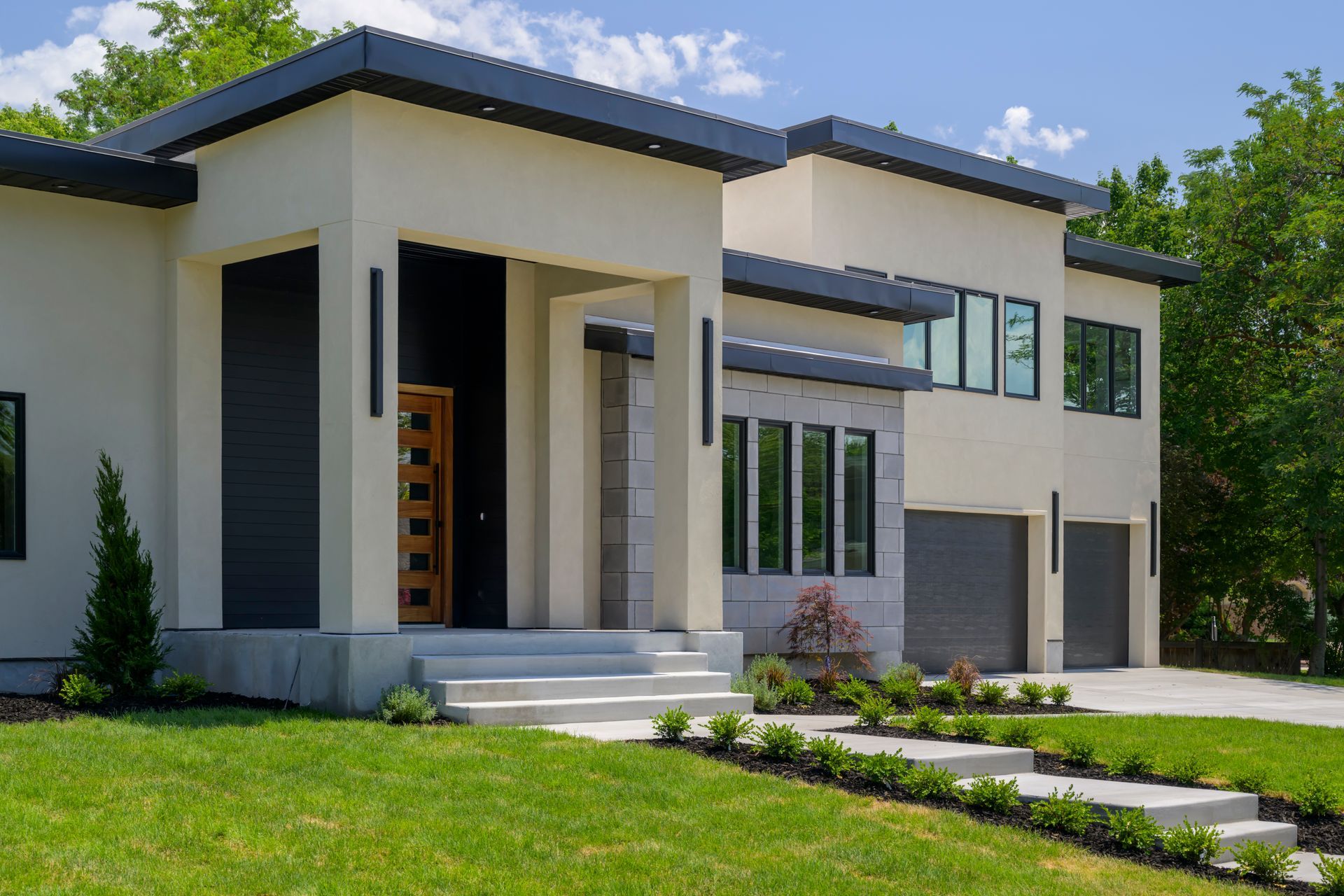 Modern two-story house with beige stucco exterior, dark trim, and a small front yard with green grass.
