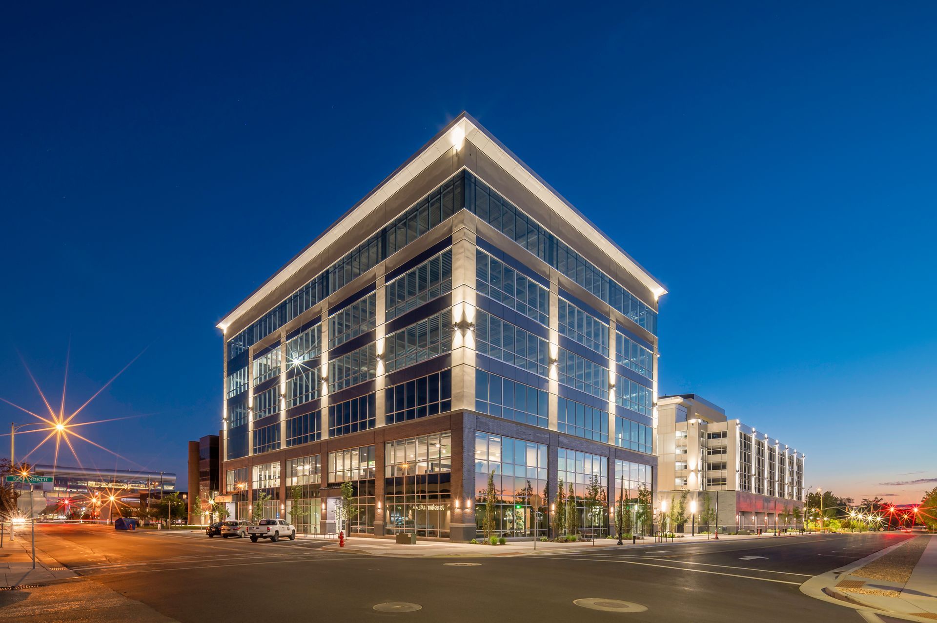 Modern glass office building lit up at dusk on a city street corner