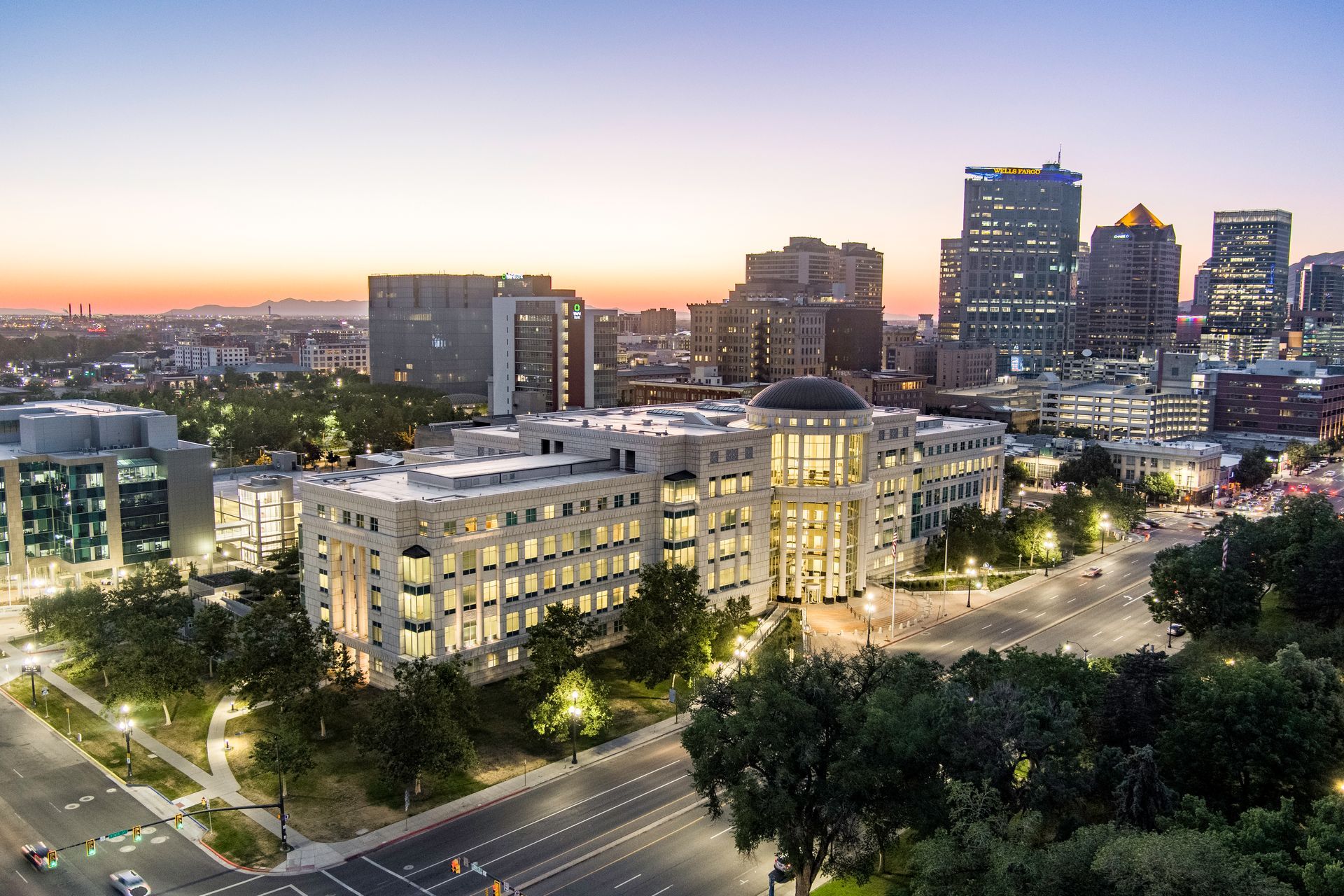 Downtown cityscape at dusk with illuminated buildings and streets under a pastel sunset sky