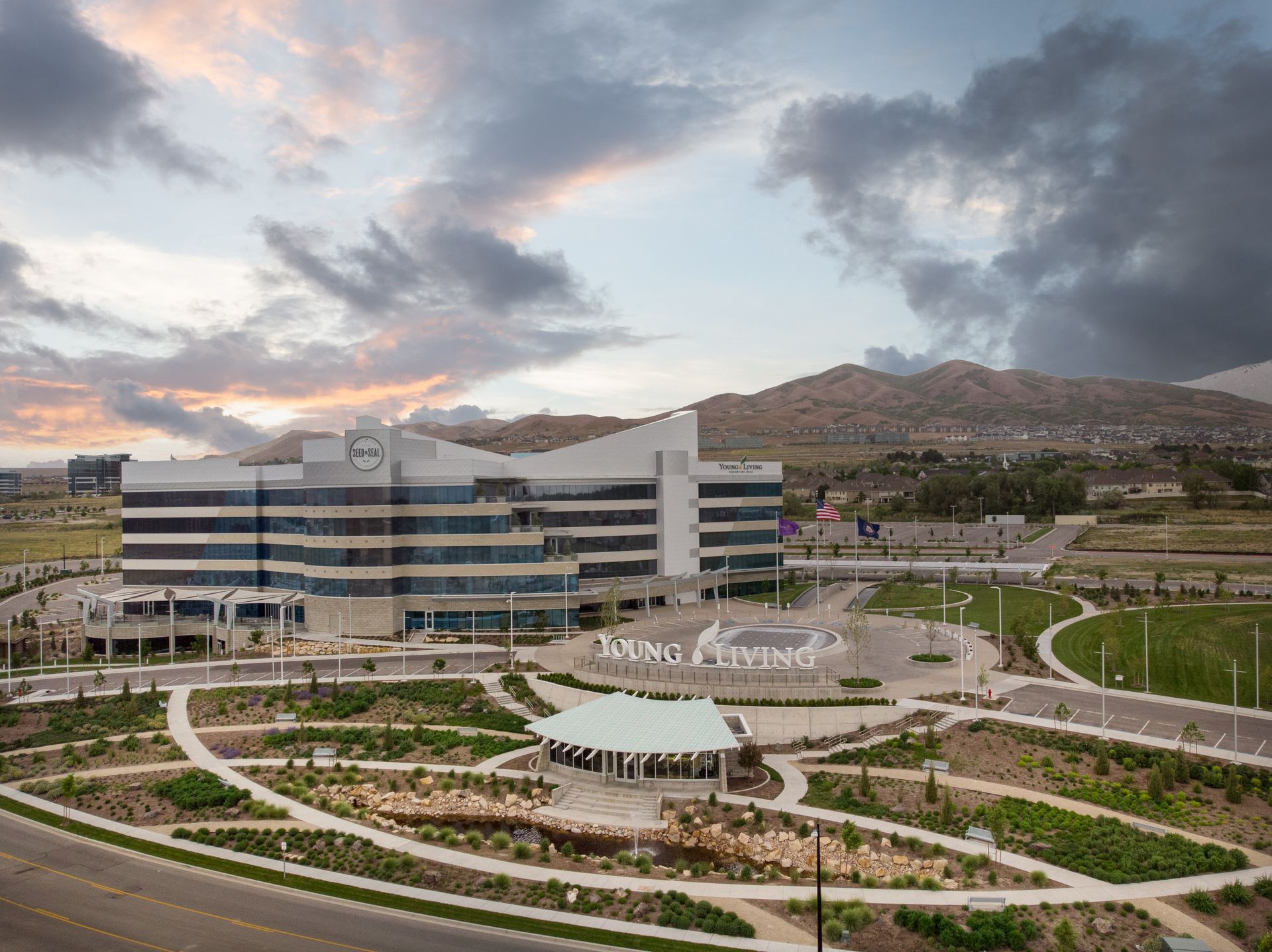 Large modern hospital complex with landscaped grounds under a dramatic cloudy sky and mountains in the background