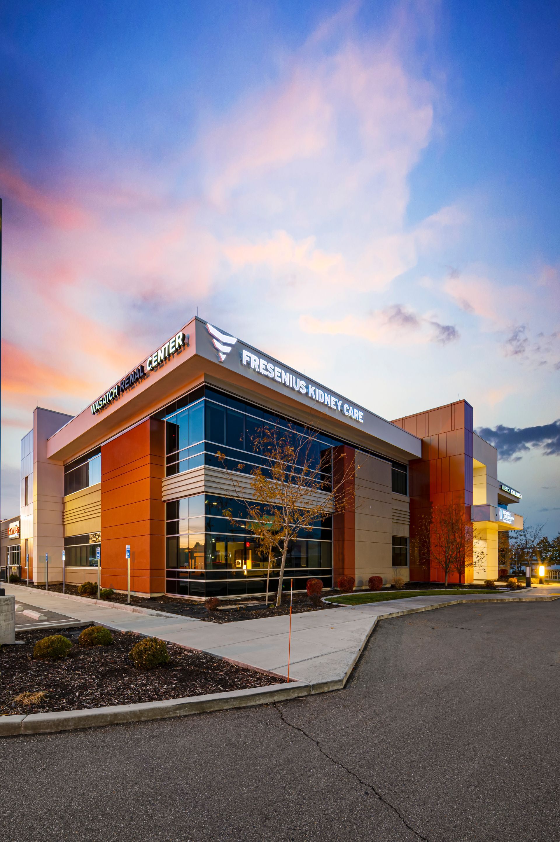 Modern brick-and-glass commercial building at dusk with warm interior lights and a pink-blue sky
