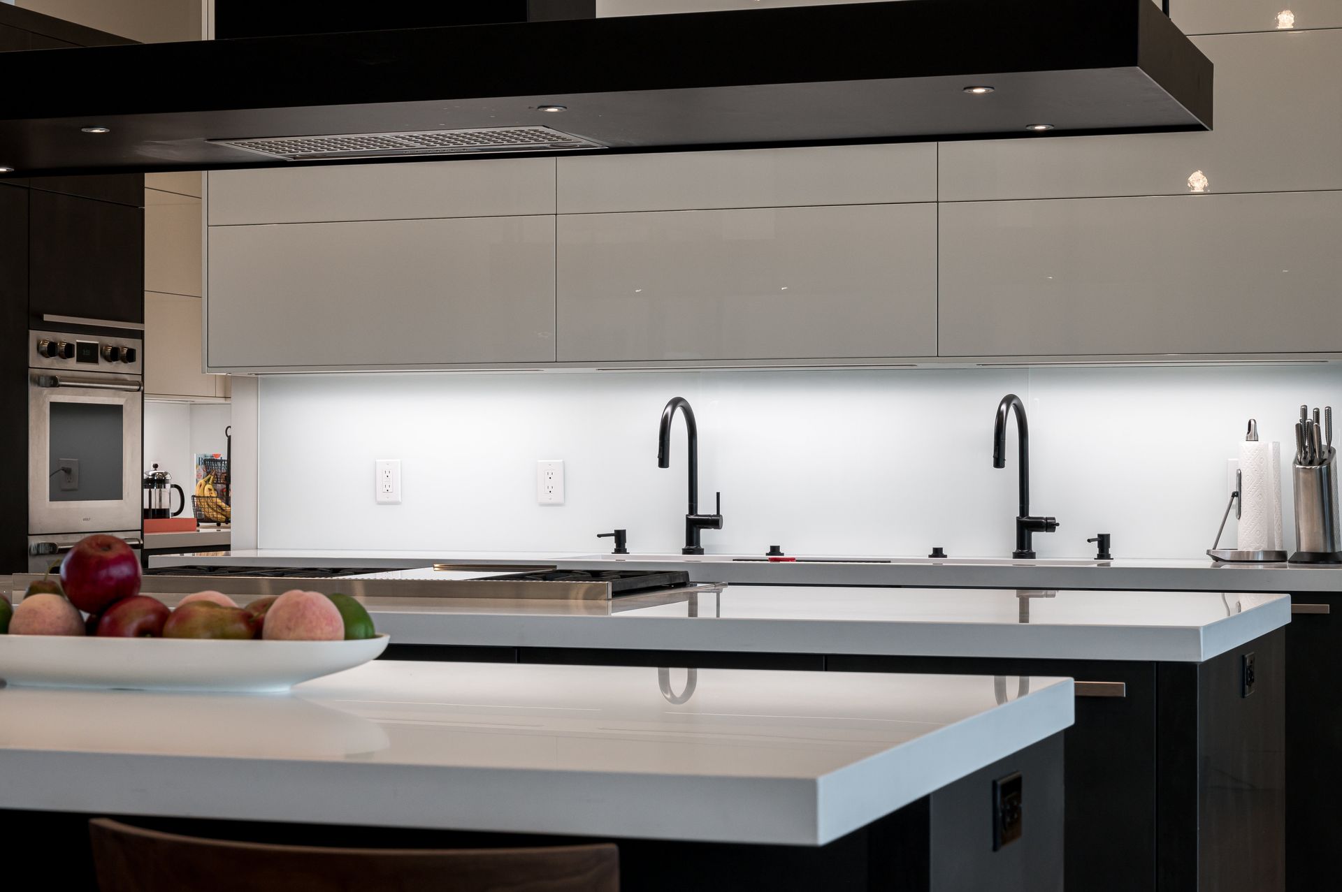 Modern kitchen with white island counters, black pendant hood, and two black faucets under sleek cabinets